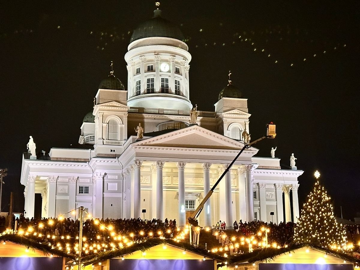 Helsinki Cathedral illuminated at night during St. Lucia Day celebration with crowds gathered at Senate Square for Tuomaan Markkinat Christmas market