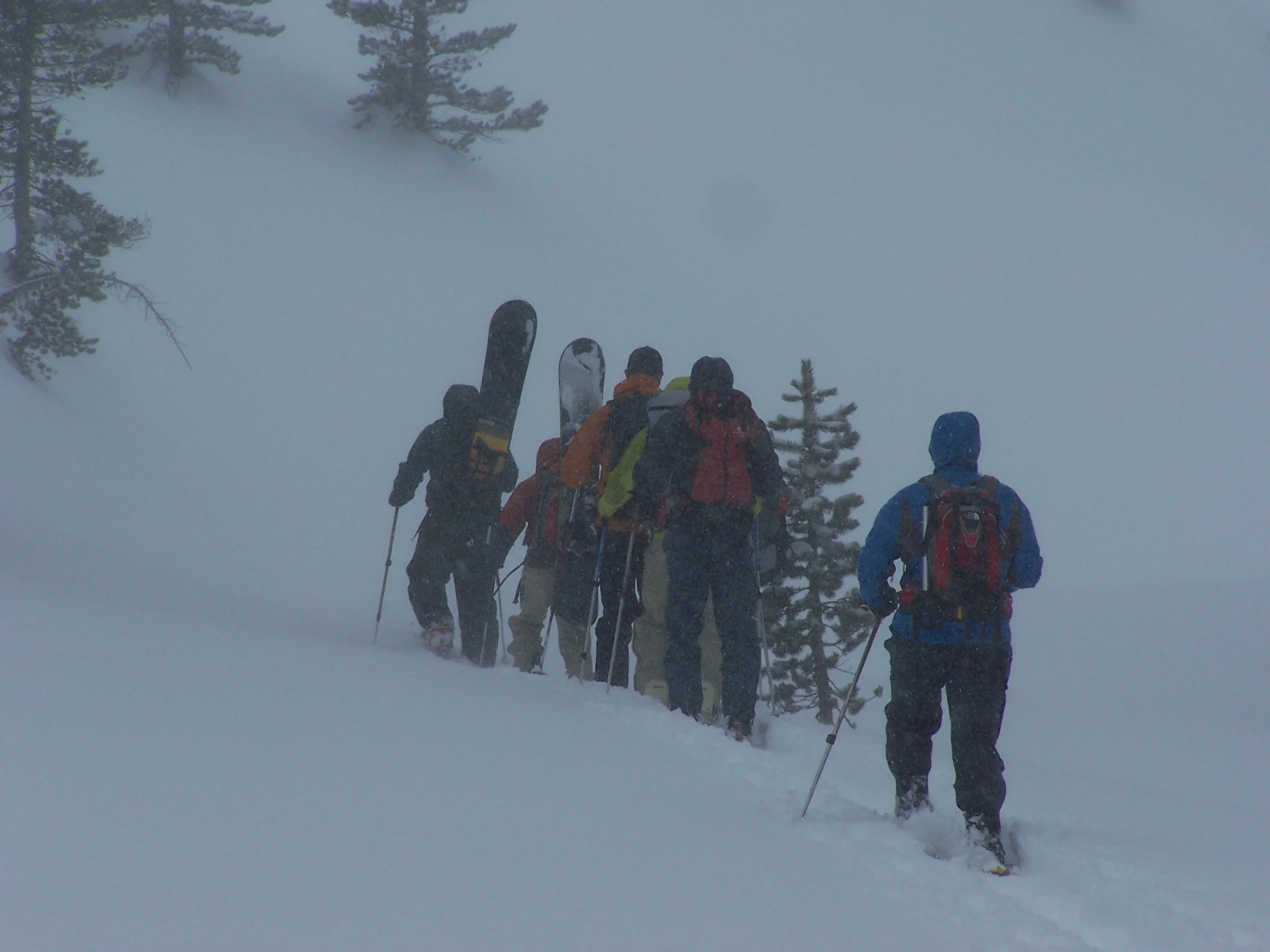 A group of people  walking in the snow while backcountry snowboarding