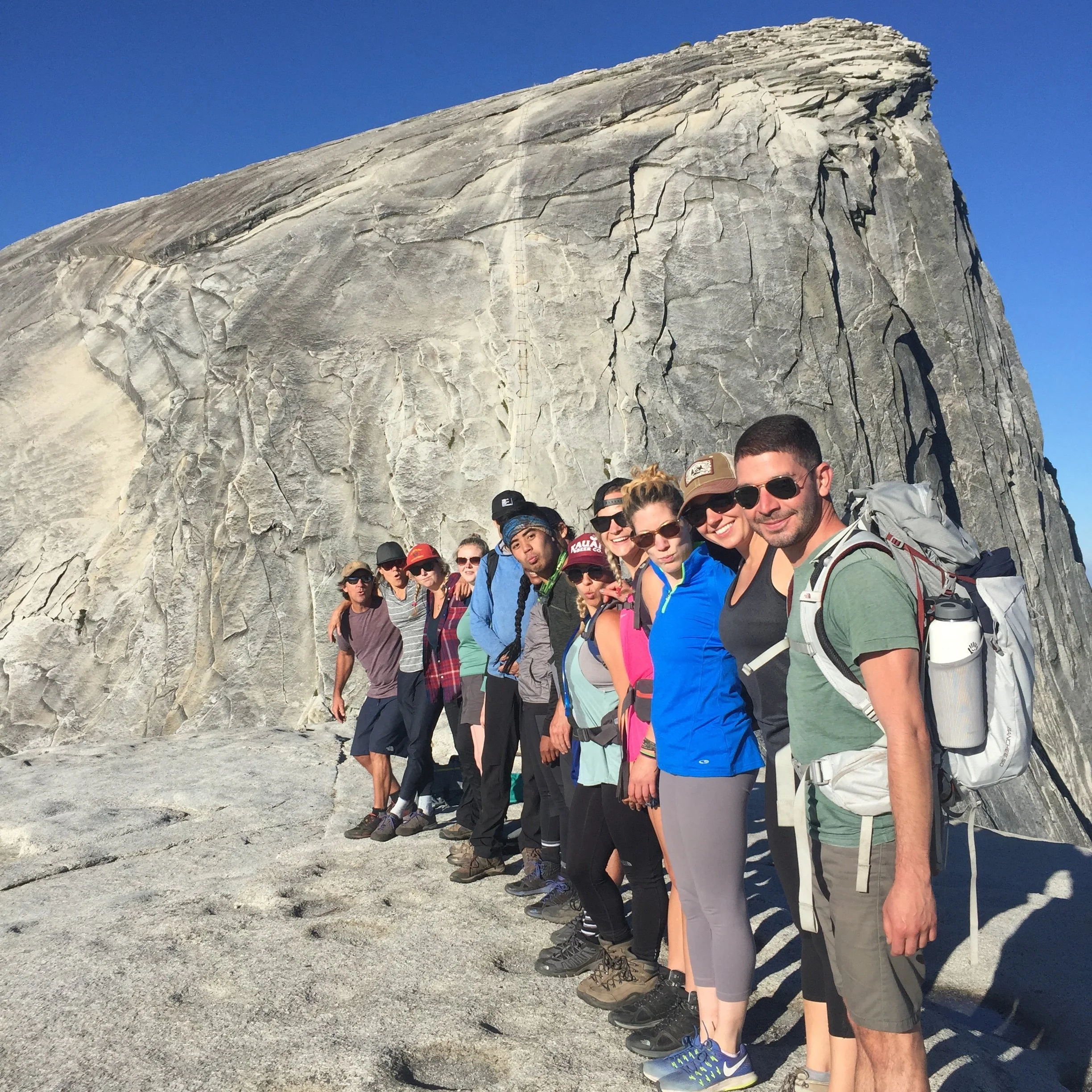 Group of hikers standing in a line with a large granite rock formation on a hiking activity.