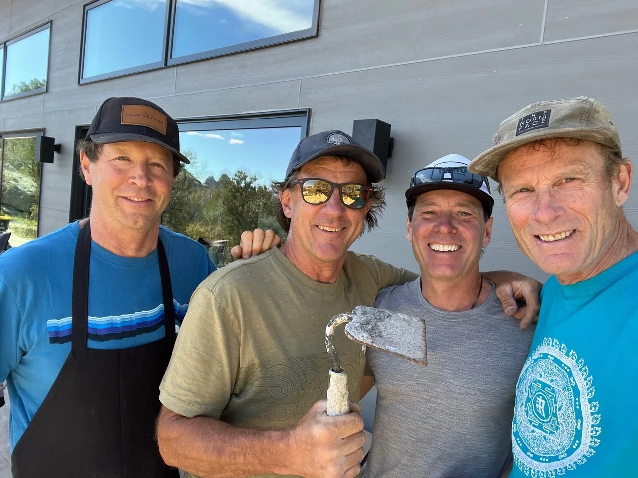 Four men smiling outdoors in front of a building