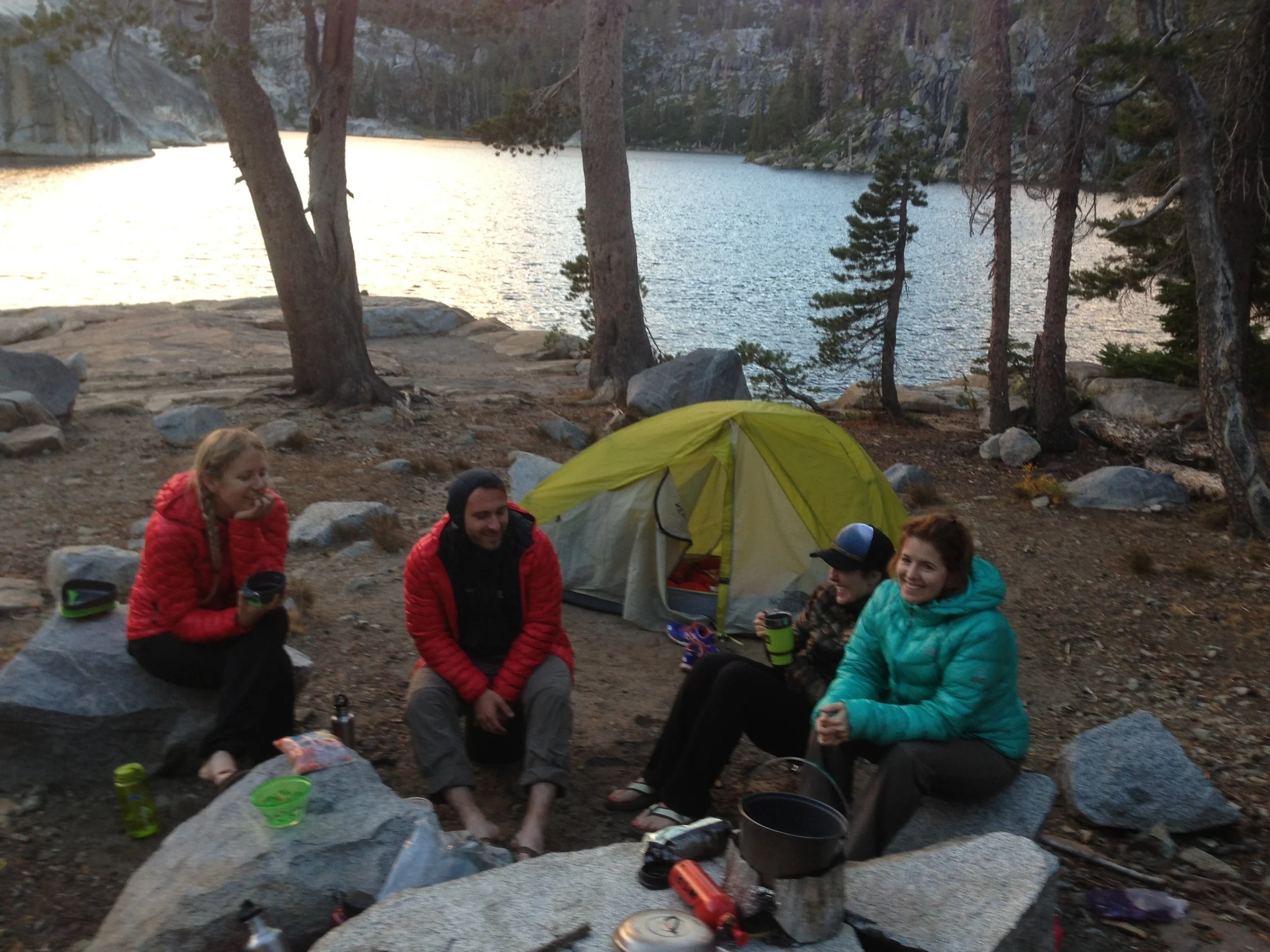 Four people sitting around a campsite near a lake on a camping activity