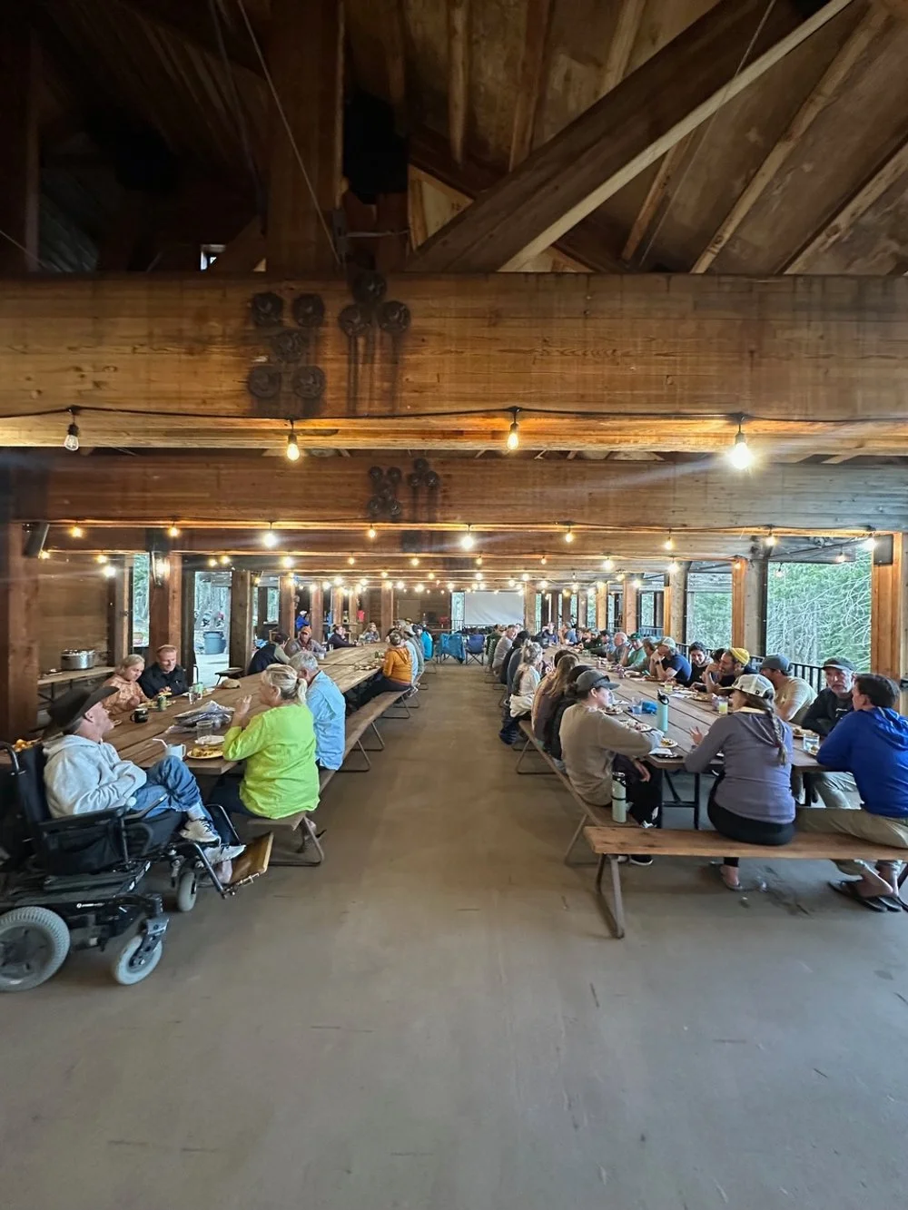 People gathered at long wooden tables in a rustic, open-air dining area