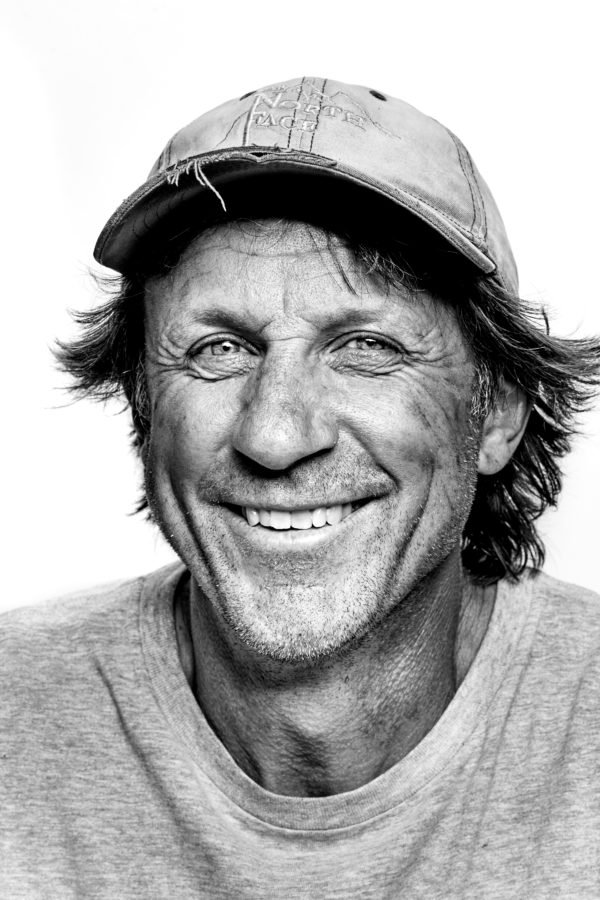 Black and white photo of a smiling man wearing a baseball cap and a t-shirt.