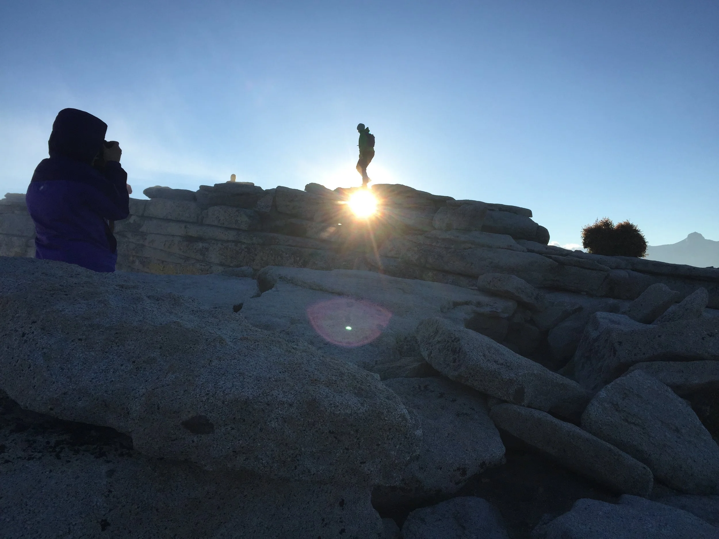 Silhouette of a person standing on a rocky formation with the sun setting behind them.