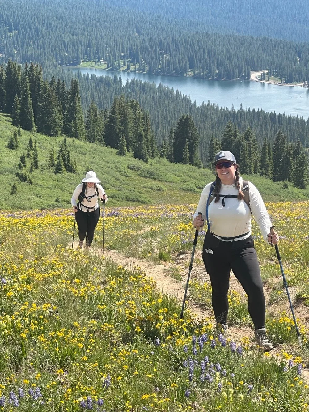 Two women hiking on a trail through a field of yellow wildflowers
