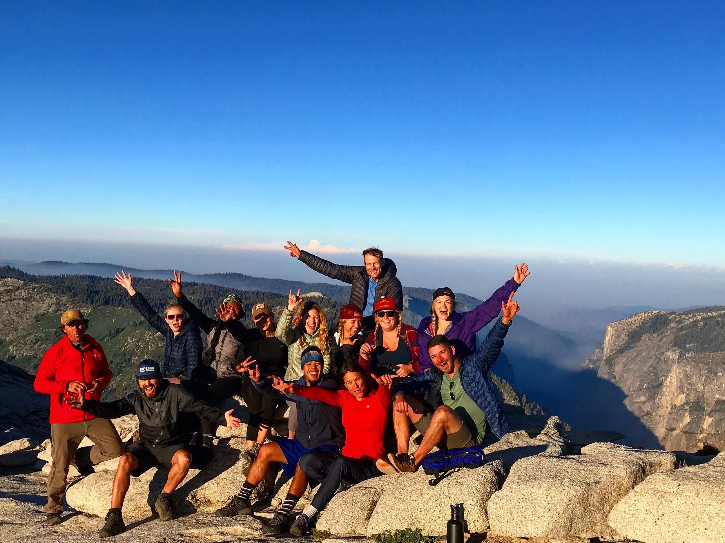 Group of people smiling and posing on a rocky mountain ledge.