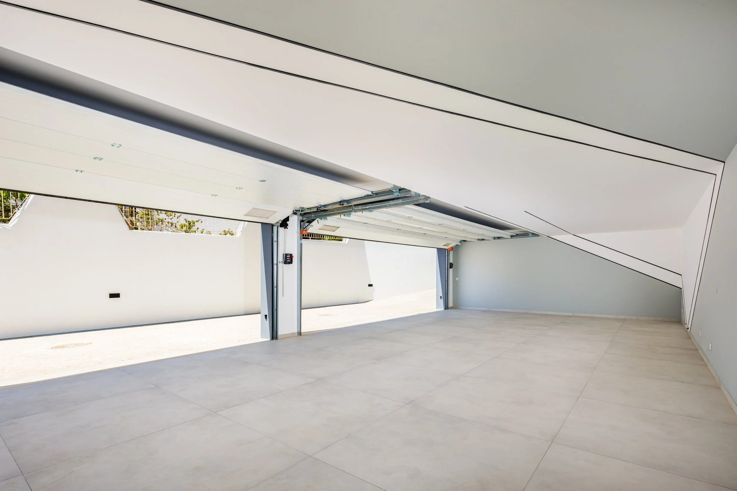 Garagem moderna com teto em inclinação, portas de fechamento automático e piso de porcelanato.