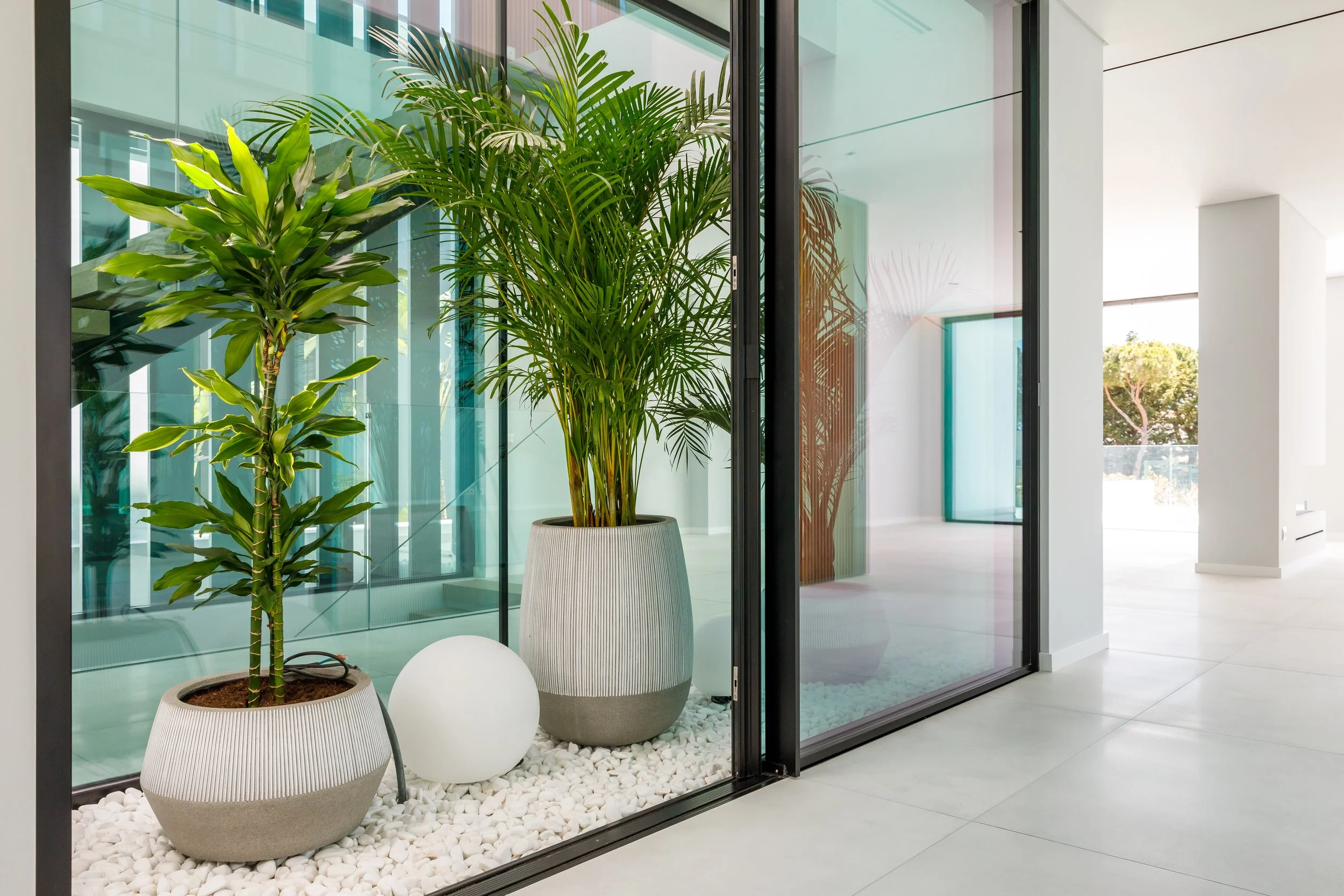 Plantas verdes em vasos decorativos dentro de um espaço moderno com piso de pedras brancas.
