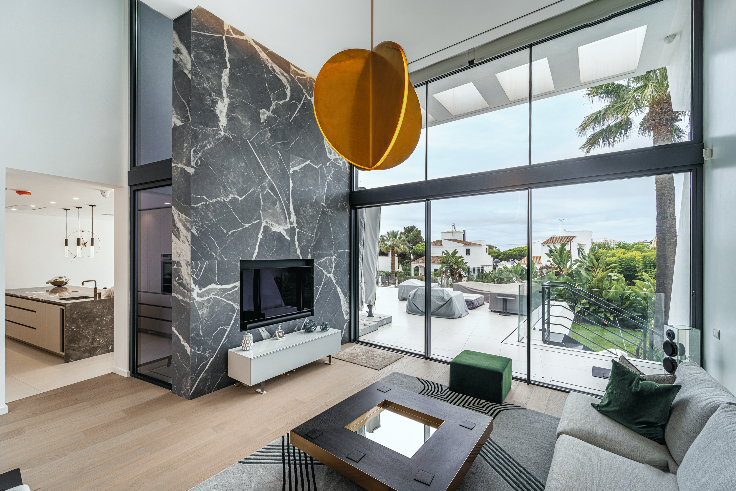 Sala de estar moderna com parede de mármore escura, televisão e janelas de vidro com vista para jardim e piscina ao ar livre.