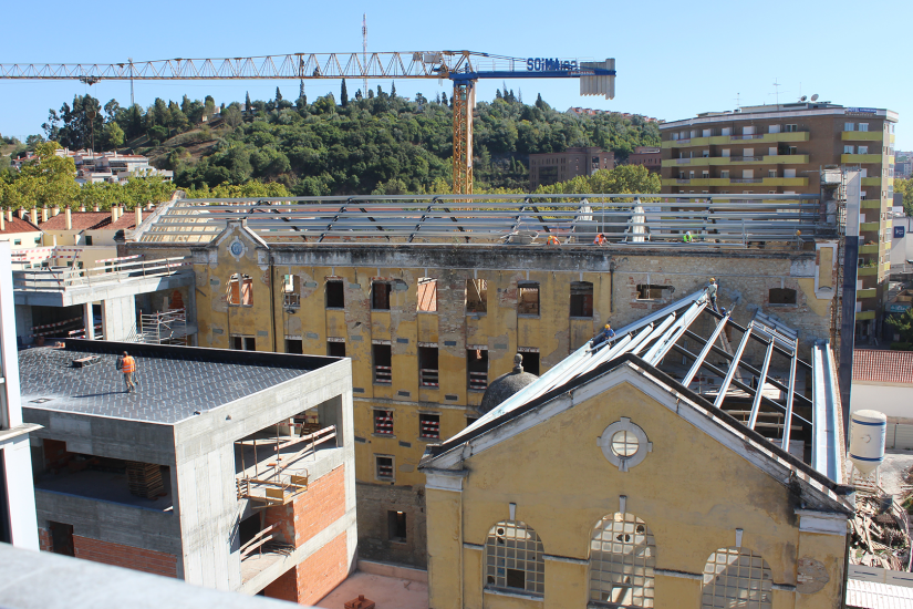 Construção de um edifício antigo com telhado em reforma, com uma grua ao fundo e trabalhadores na obra.
