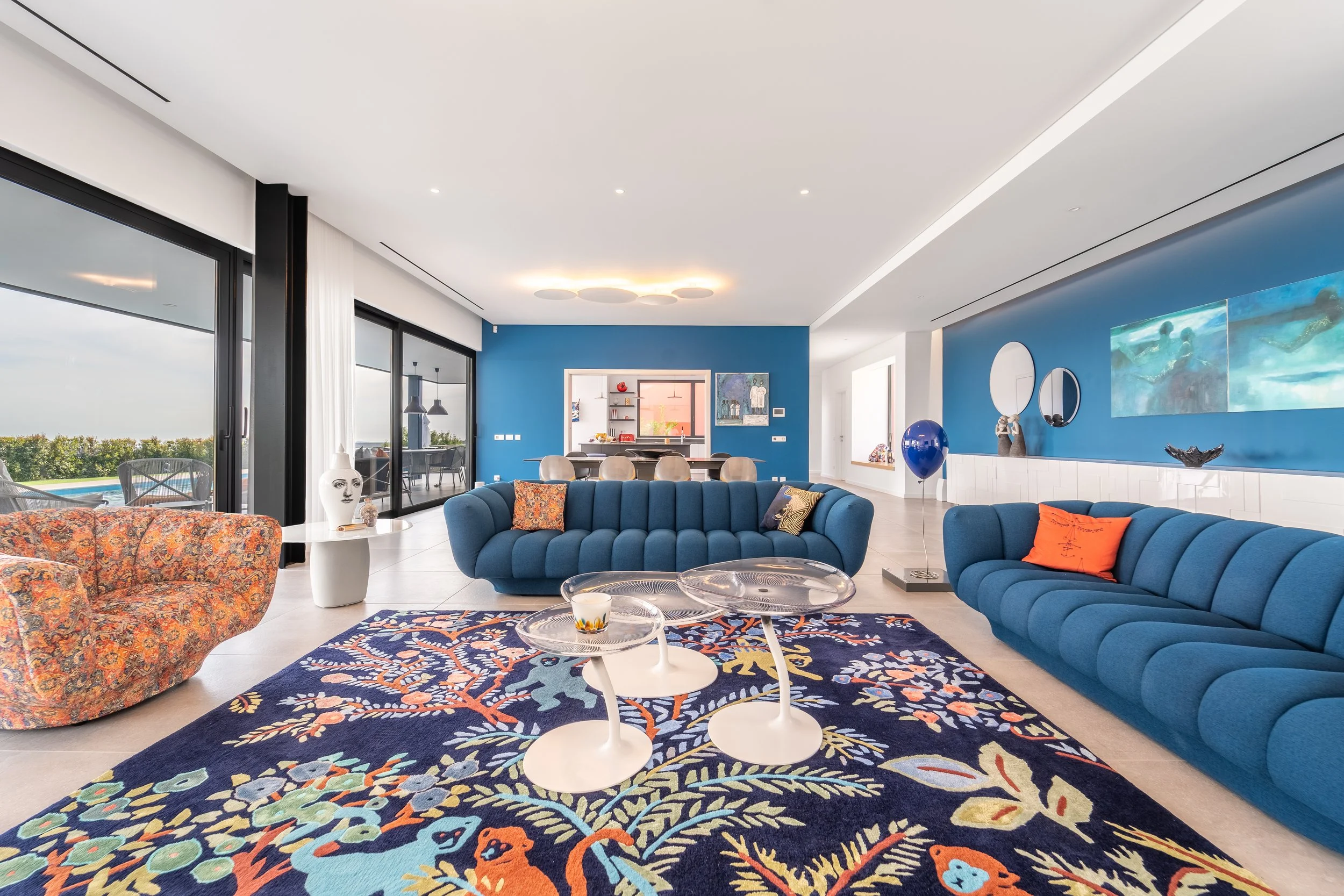 Sala de estar moderna com sofá azul, luminária decorativa e tapete colorido, com vista para varanda ao ar livre.