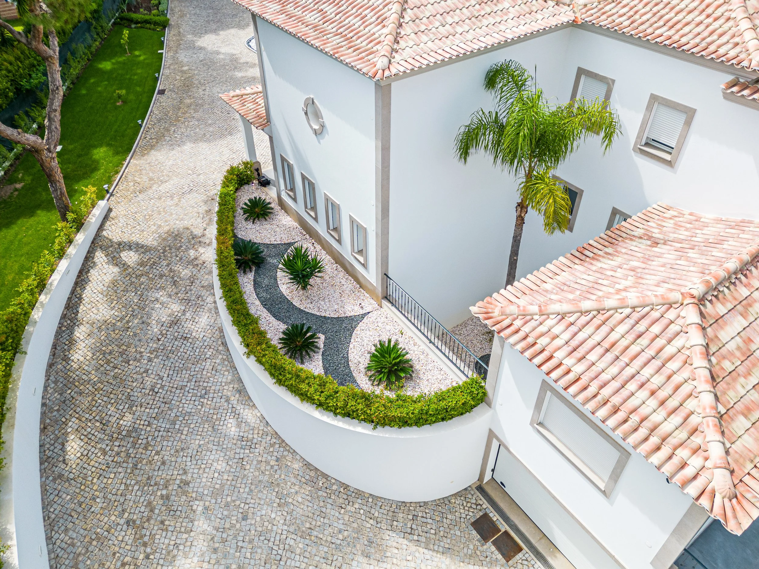 Vista aérea de uma casa com telhado de telhas de barro, paredes brancas, jardim com plantas e caminho de pedras.