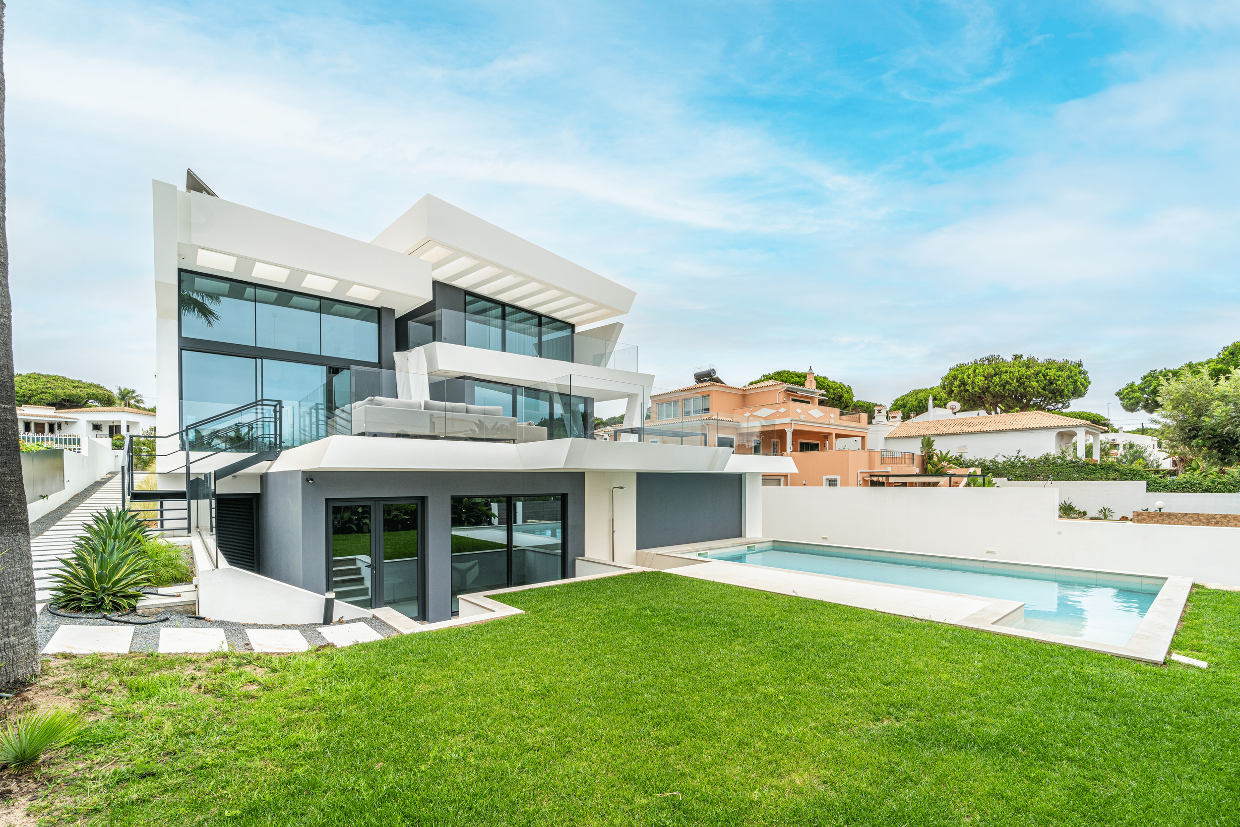 Residência moderna com fachada de vidro, área de piscina e jardim bem cuidado sob céu nublado.