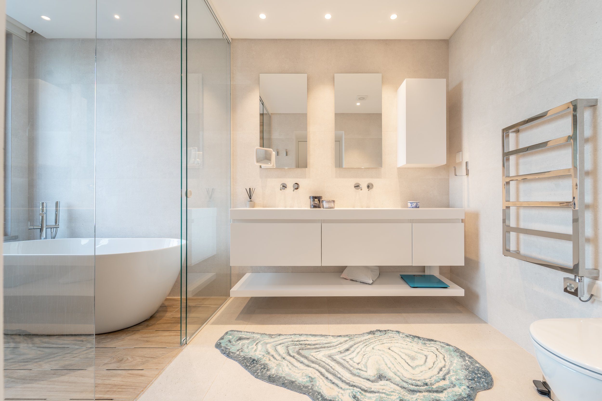 Banheiro moderno com bancada dupla, espelhos, banheira de hidromassagem, toalheiro de metal, e tapete na frente da pia.