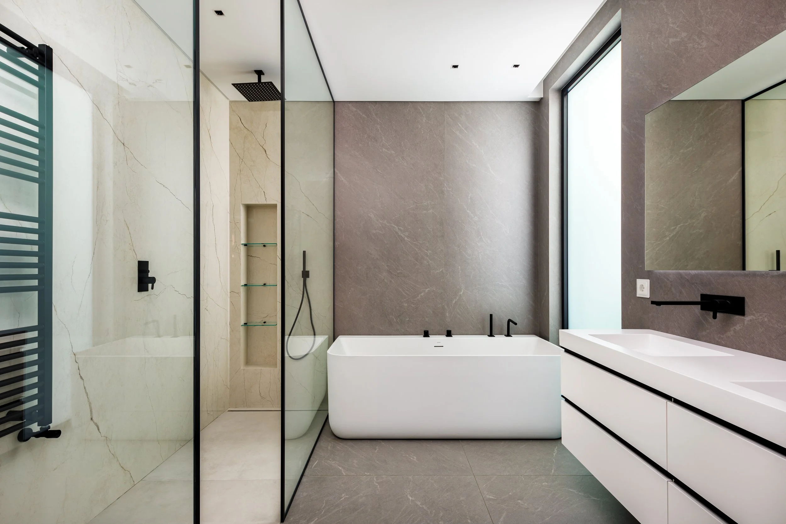 Banheiro moderno com ducha, banheira, vaso sanitário, pia branca com espelho grande e janelas de vidro.