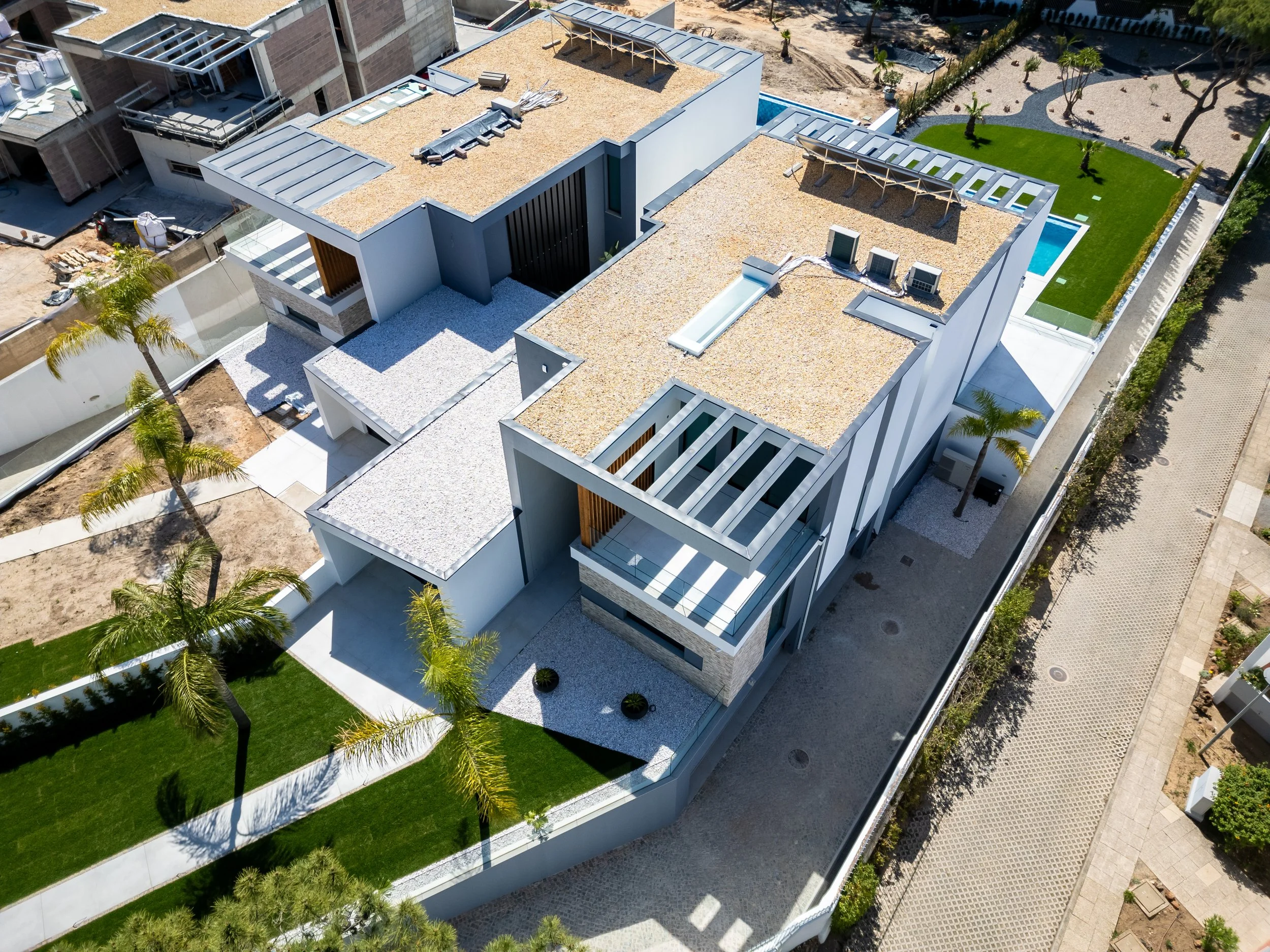 Vista aérea de uma casa moderna com telhado de telhas de passagem, área de piscina, jardim bem cuidado com gramado, árvores e caminhos pavimentados ao redor.
