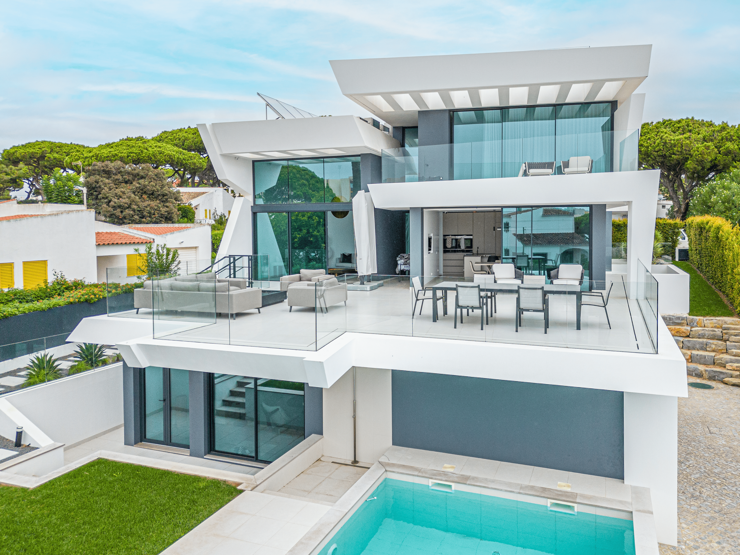 Casa moderna com terraço, piscina e área de convivência ao ar livre, com móveis de lazer e grandes janelas de vidro.