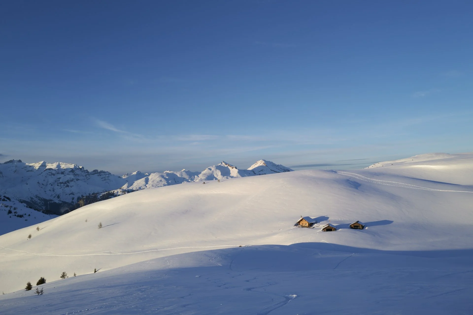 Aussicht auf die Hütten von Culm Ault und dem Dreibündenstein in einer winterlichen Landschaft bei Sonnenuntergang. Kein Windpark Dreibündenstein
