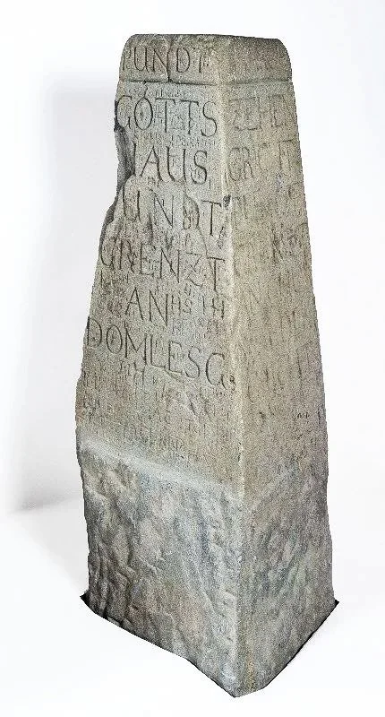 Stein mit eingravierten lateinischen Schriftzeichen.  Calma Grischun, Kein Windpark, Windpark Nein, Dreibündenstein, Domleschg, Churwalden, Chur, Windenergie, Axpo.