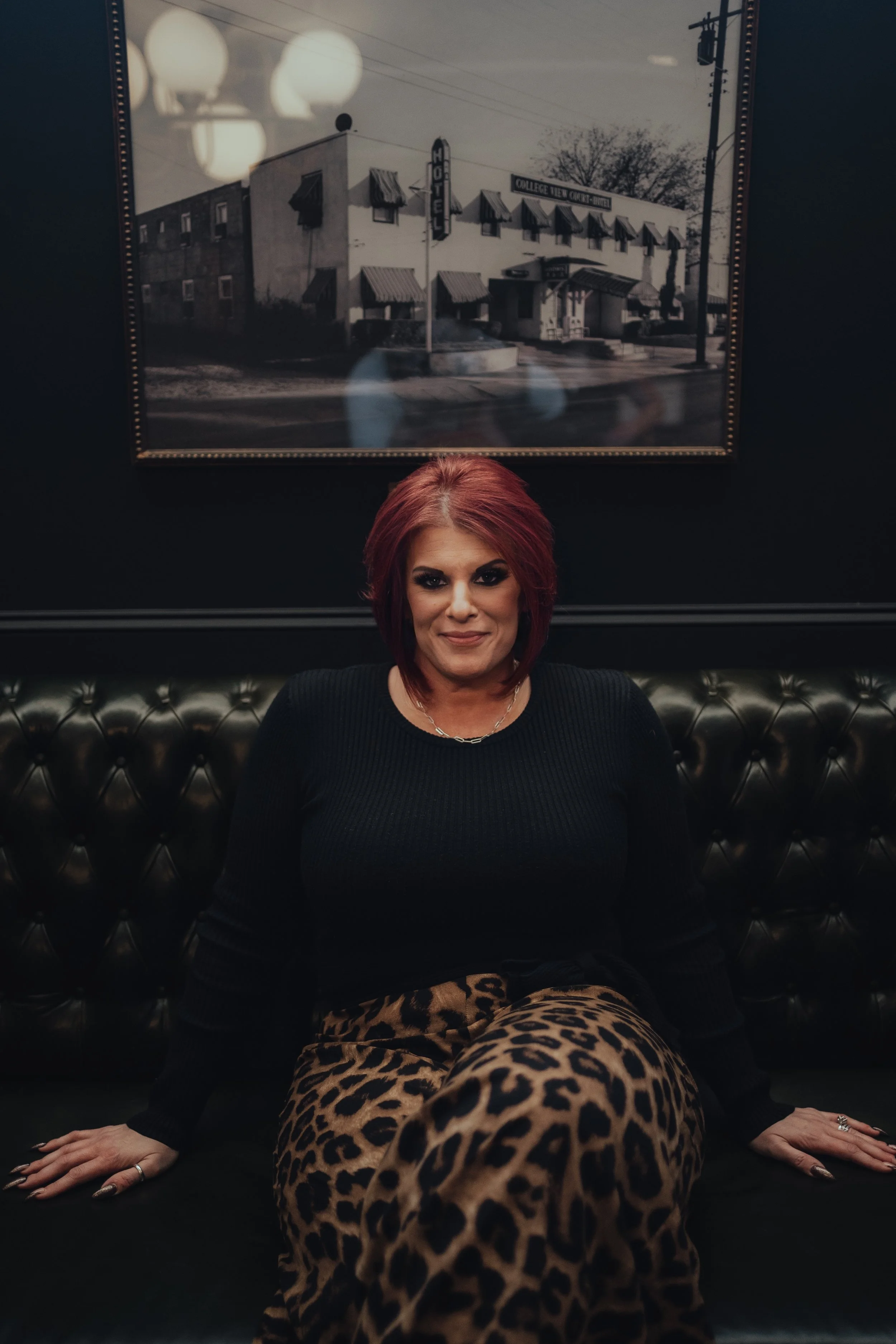 Amber Brown, Founder of White Label Training, sitting on a black leather couch, wearing a black top and leopard print pants, in the library of Hotel 1928 in Waco.