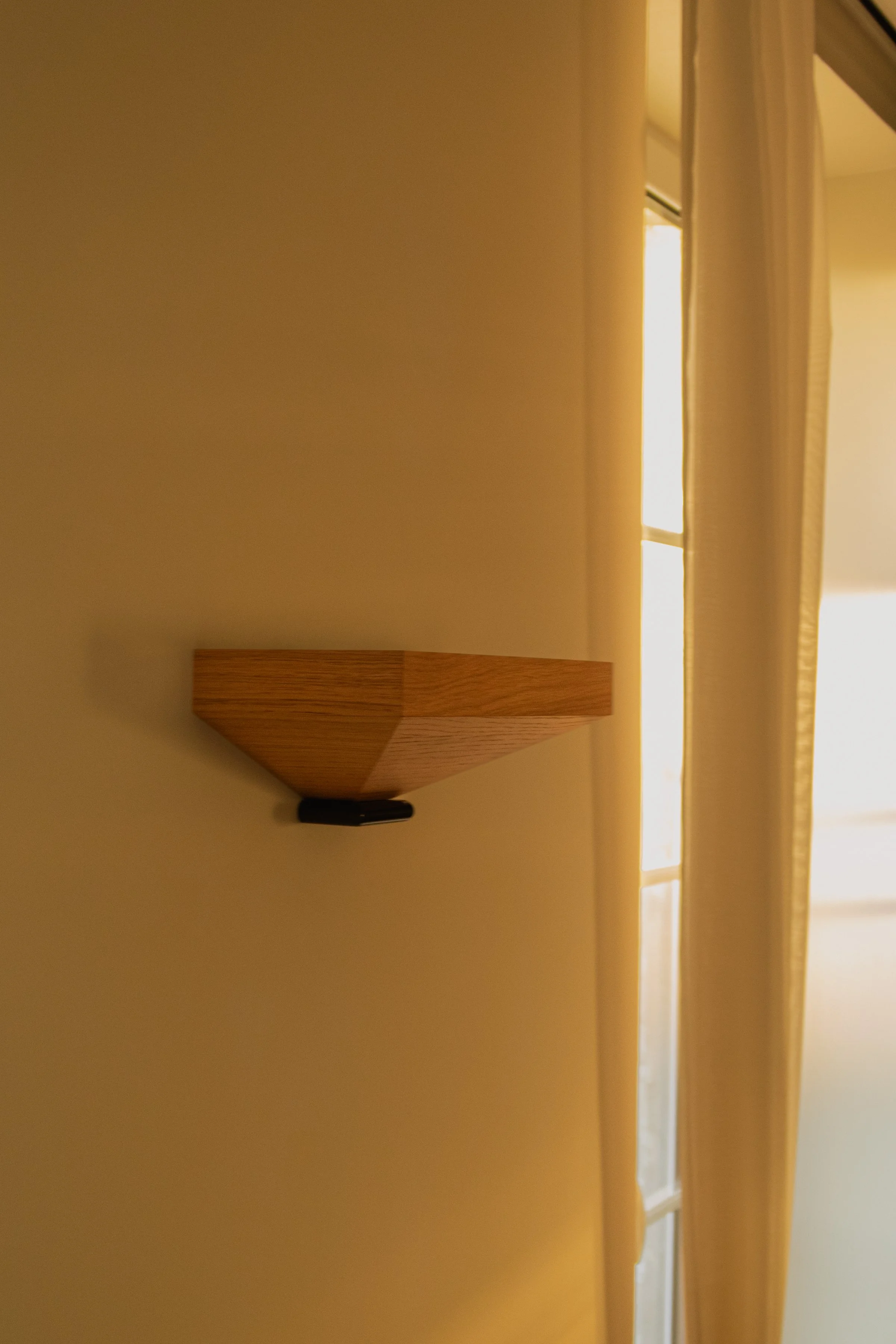 Une applique morte en bois fixée à un mur jaune, avec une fenêtre et des rideaux en tissu clair à proximité.