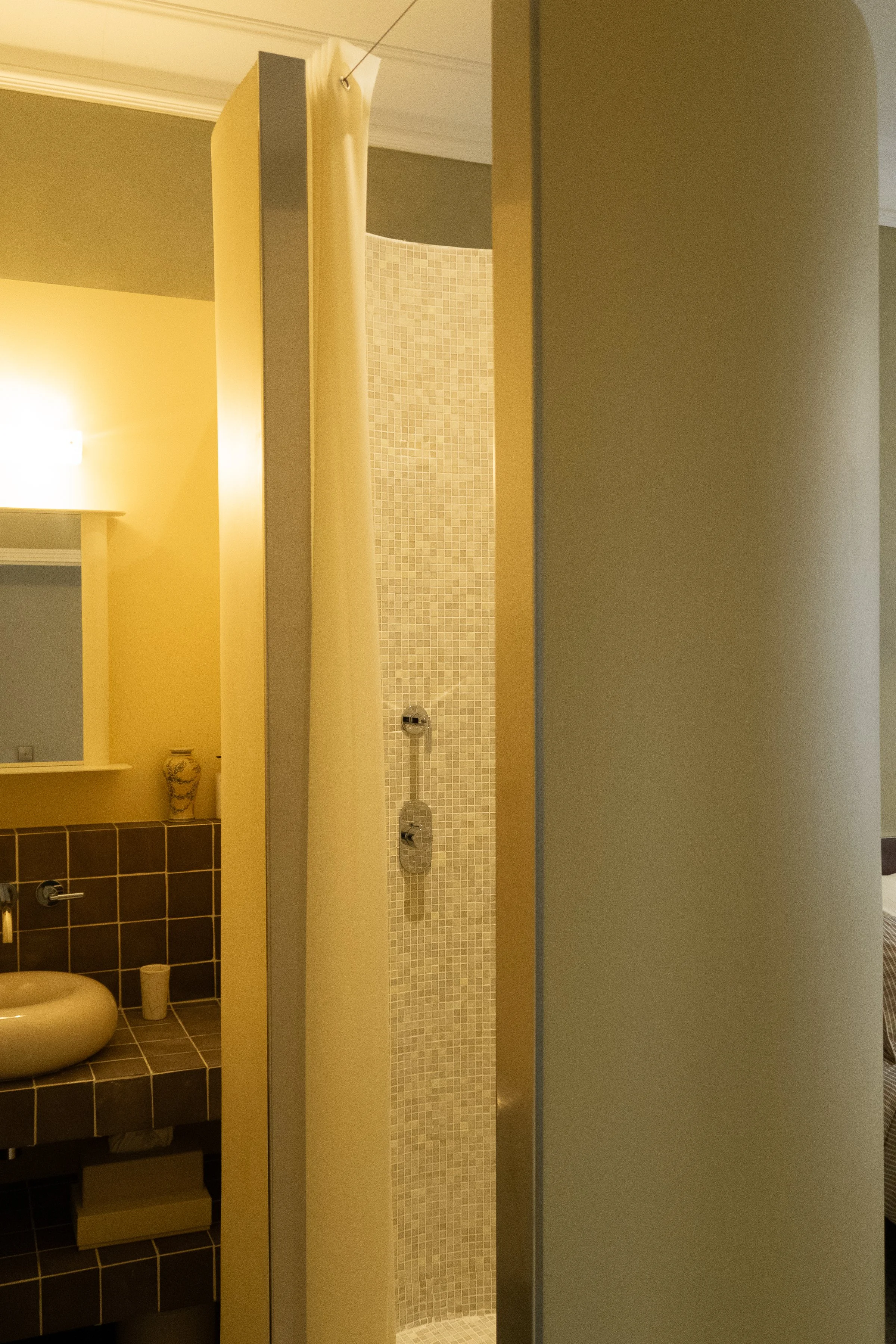 Vue partielle d'une salle de bain avec une douche, un lavabo et un miroir, dans une pièce lumineuse.