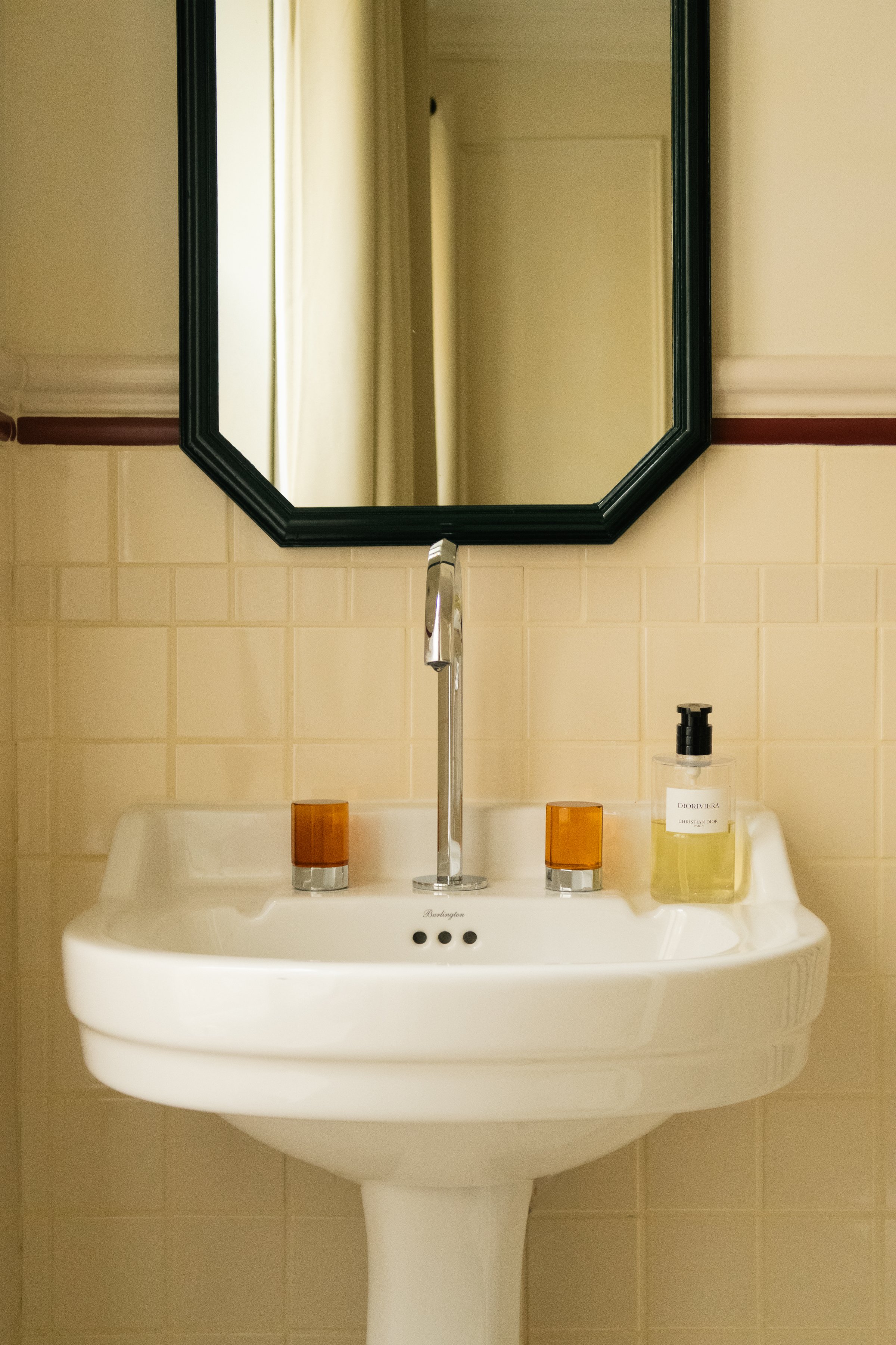 Lavabo blanc avec miroir, deux gobelets en verre orange, flacon de savon liquide sur un mur carrelé beige