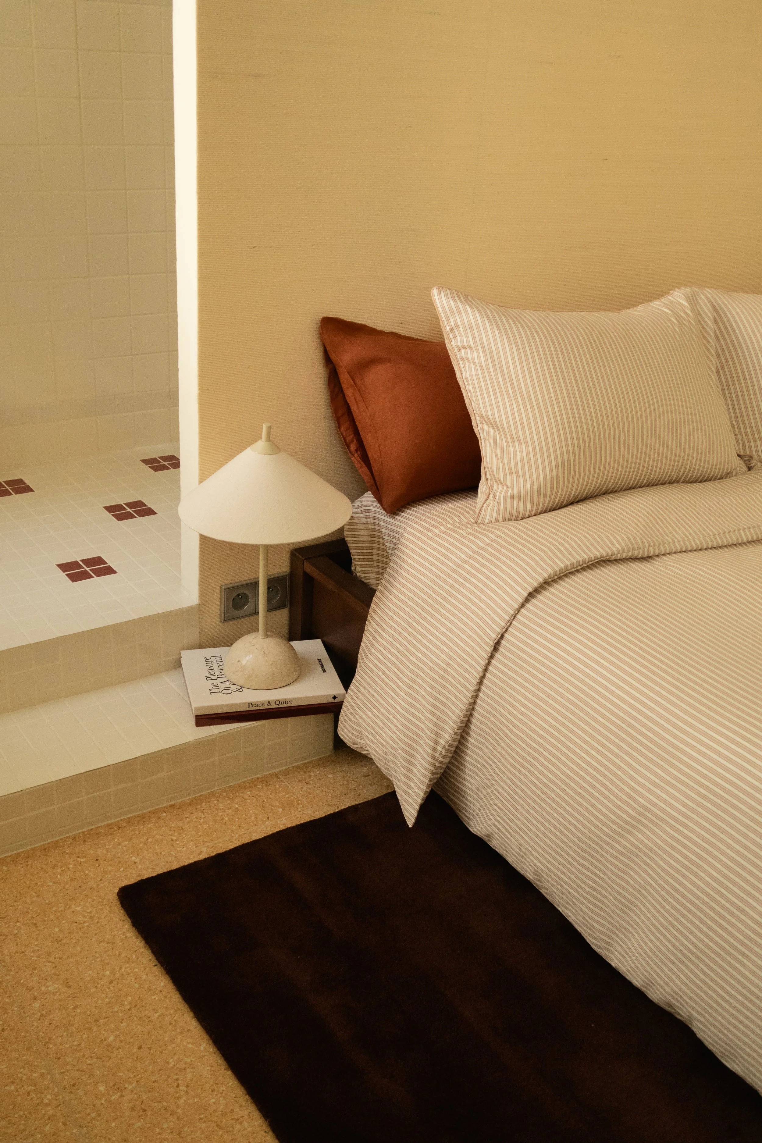 Lit avec oreillers, table de chevet avec lampe et livres, accès à une salle de bain dans une chambre d'hôtel.