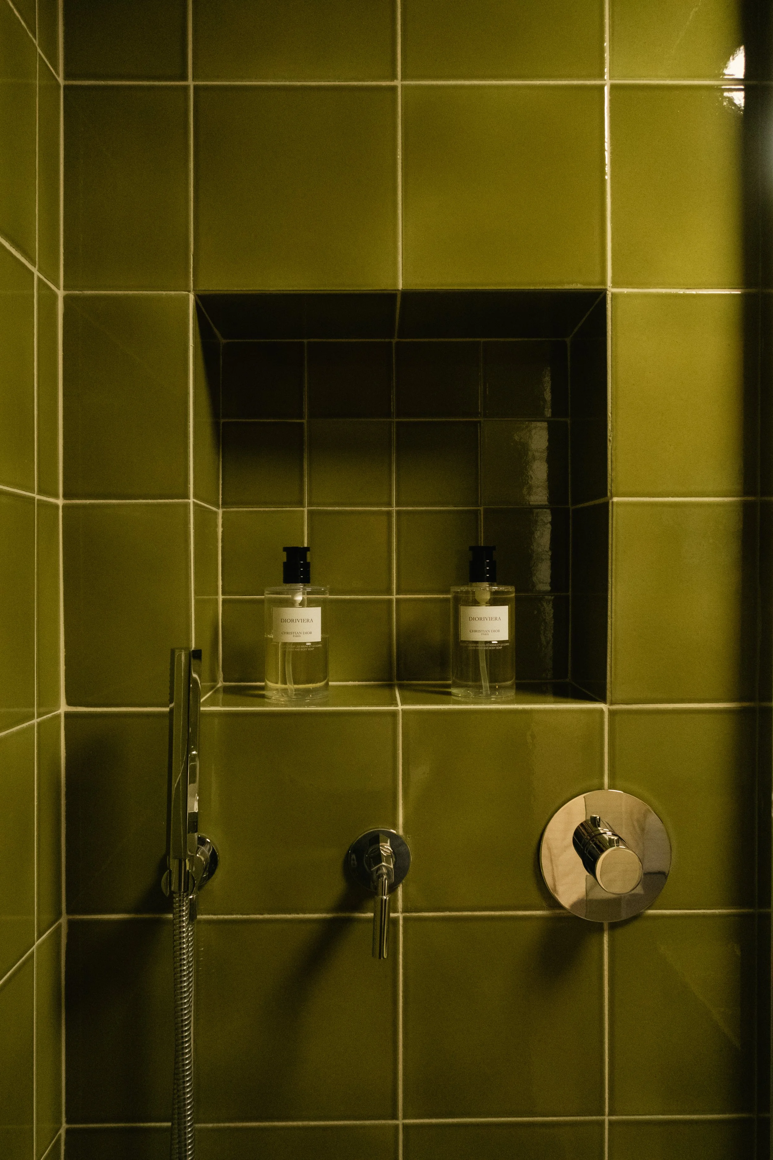 Vasque de douche avec deux bouteilles de savon ou shampoing dans une niche intégrée, les murs sont recouverts de carreaux verts.
