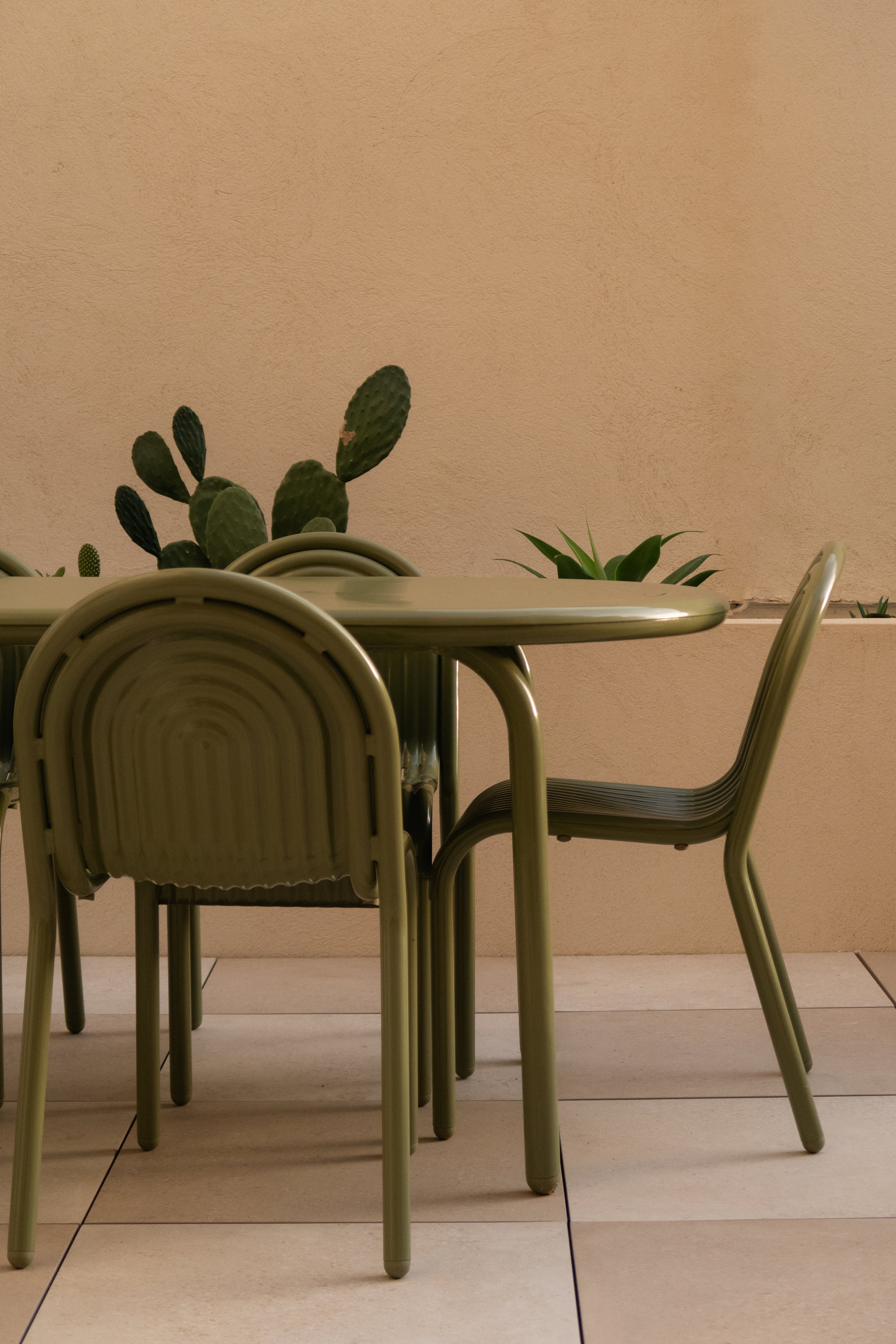 Chaises d'extérieur en métal vert autour d'une table, fond de mur beige avec plantes cactus et succulentes.