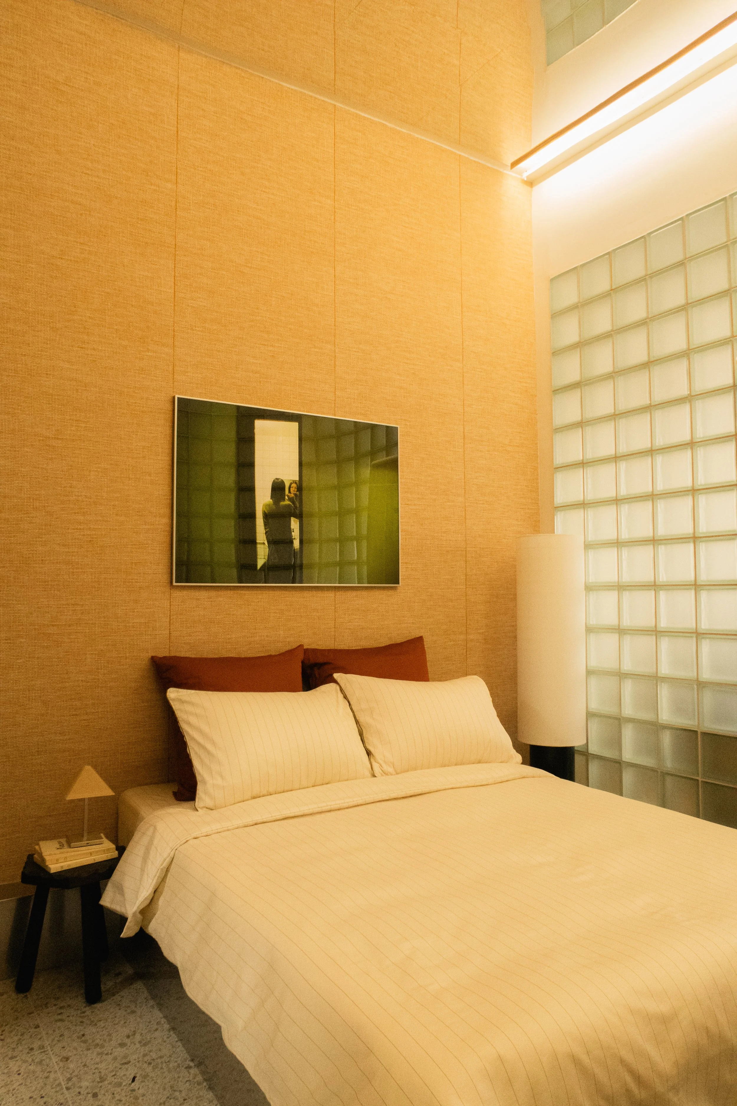 Chambre d'hôtel avec lit double, coussins marron et crème, table de nuit avec des livres, lampe de chevet et un grand miroir