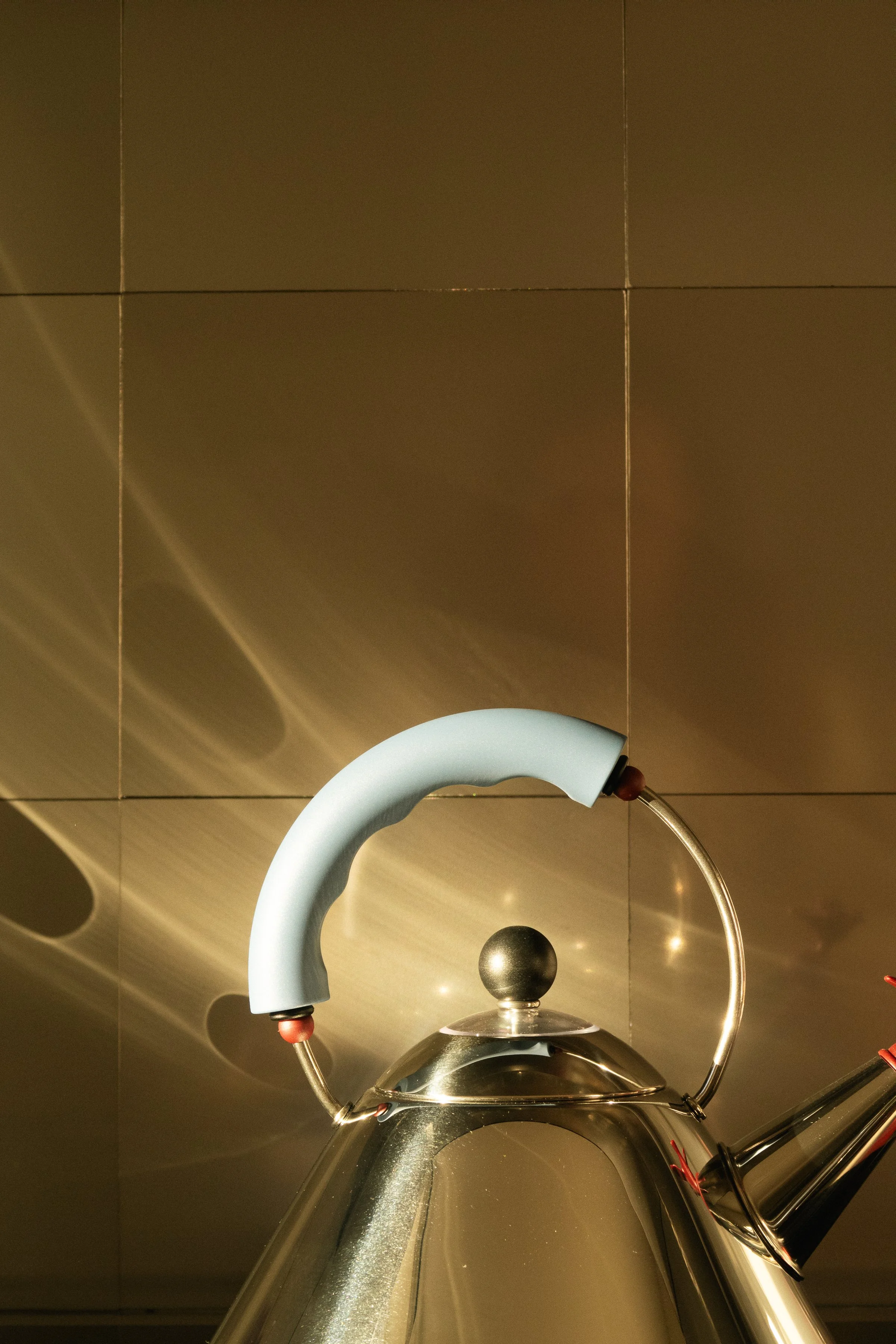 Une bouilloire en acier inoxydable avec une poignée en plastique bleu et un bouton noir sur le couvercle, placée devant un mur en carrelage marron.