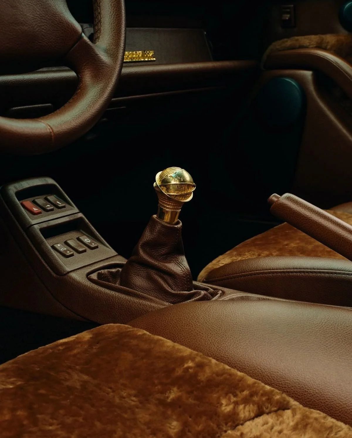 Intérieur d'une voiture avec levier de vitesse en métal doré, tableau de bord en plastique brun et sièges en tissu beige avec motifs.