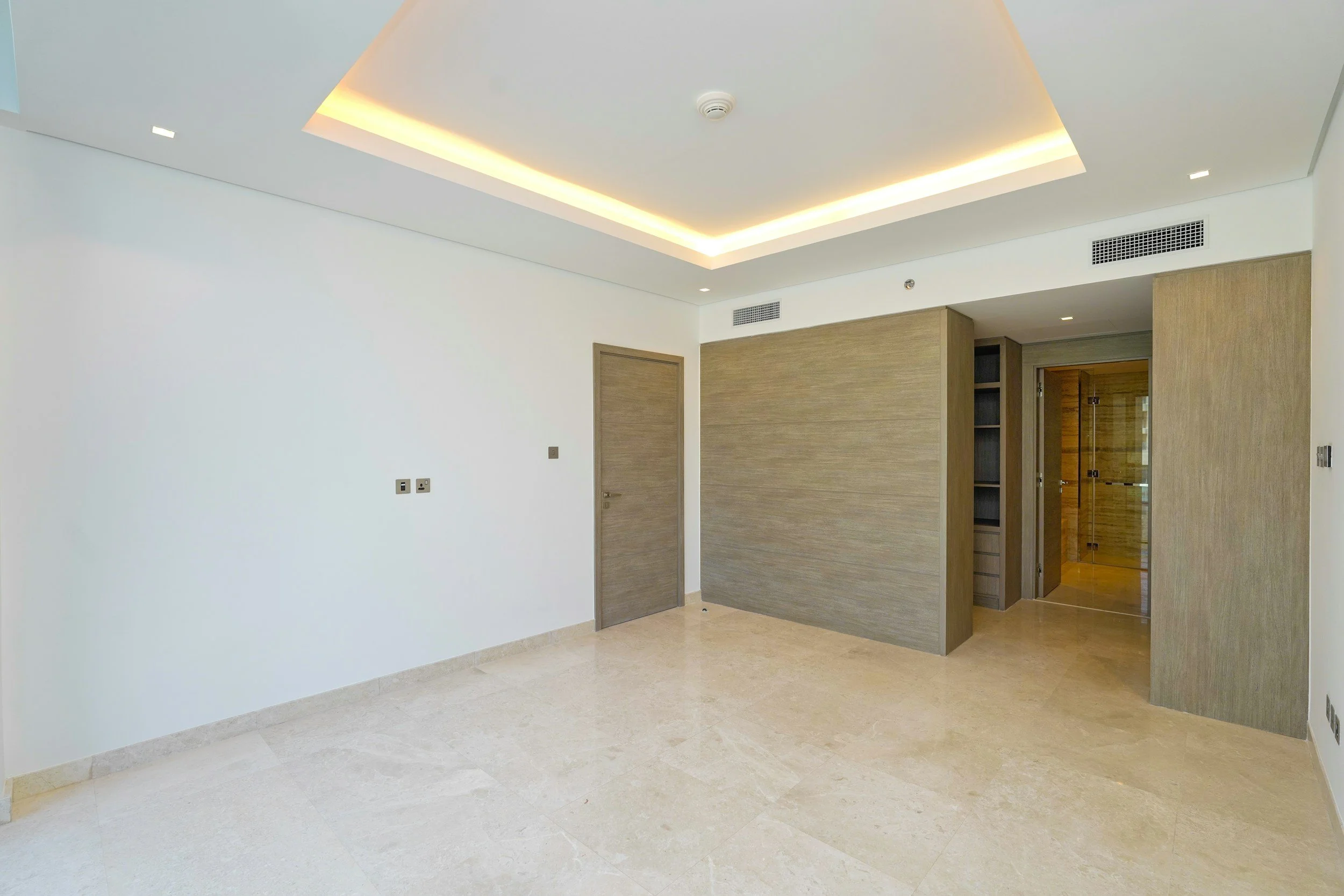 Empty modern room with white walls, beige marble floor, wooden doors, and recessed ceiling lighting.