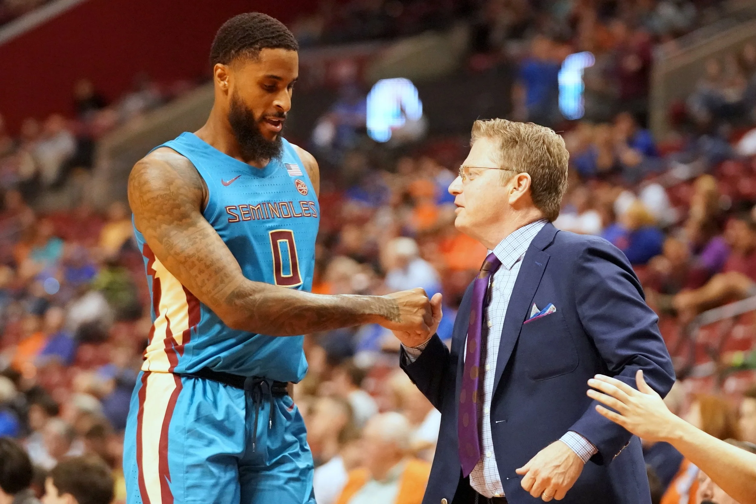 A basketball player in a blue Florida State Seminoles jersey shakes hands with a man in a suit at a basketball game.