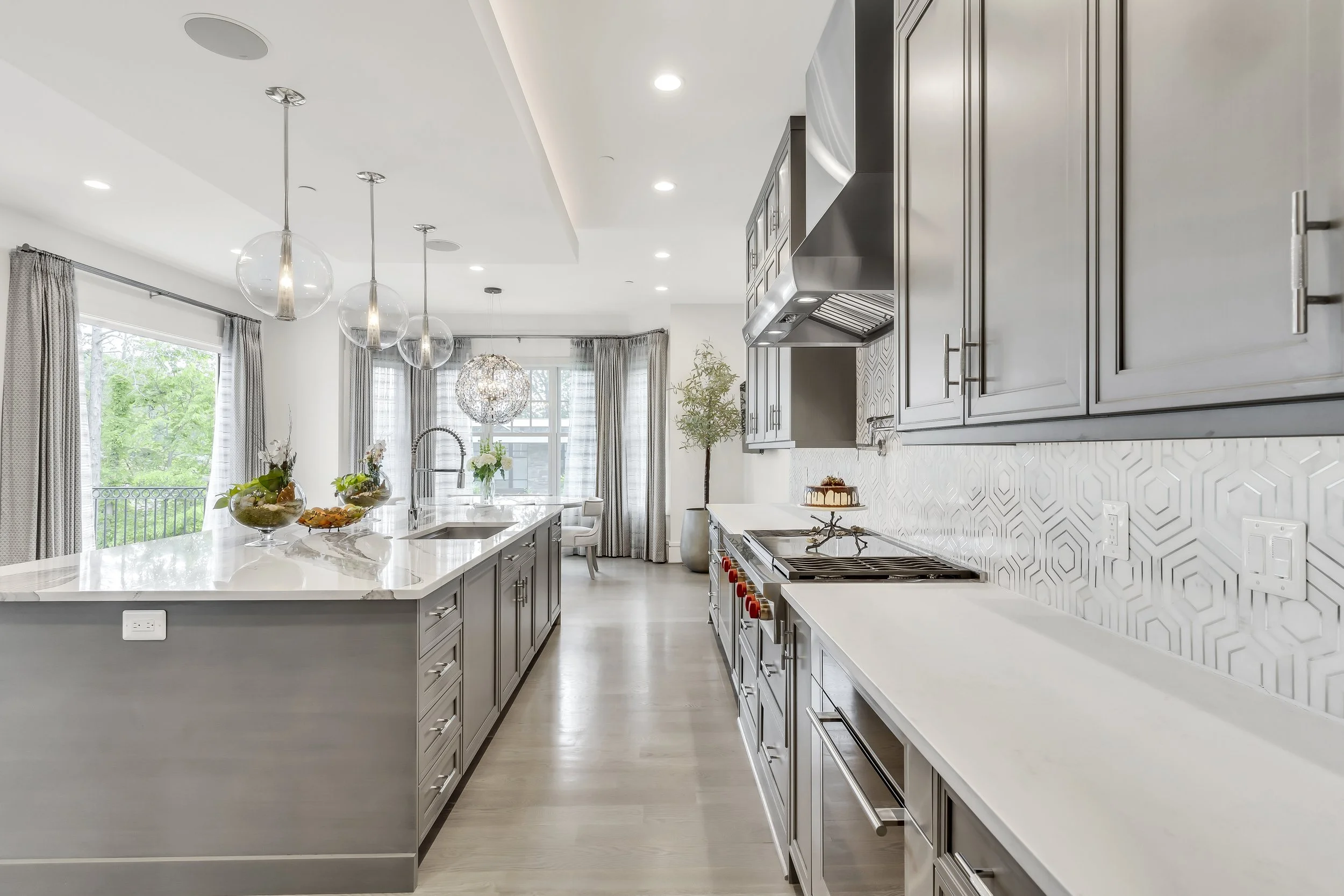 Modern kitchen with gray cabinets, white countertops, and pendant lights, with a vanishing point showing a dining area with large windows and curtains.