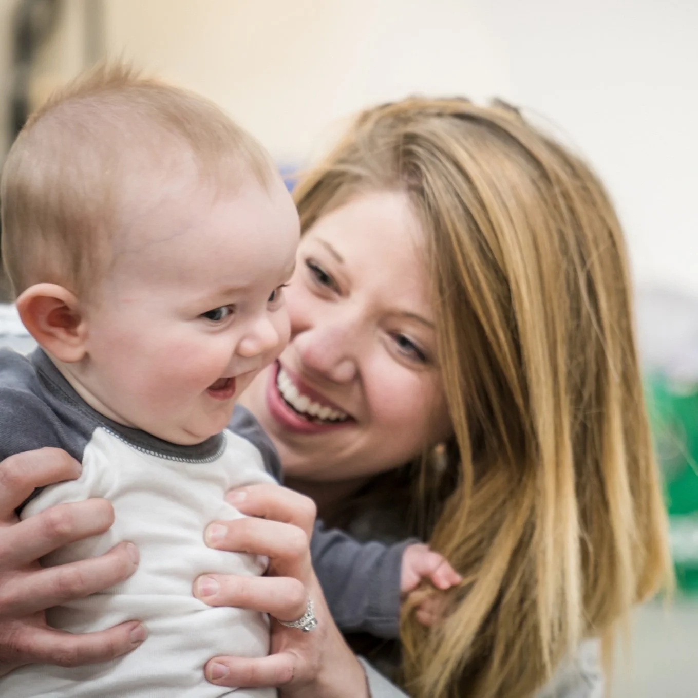 A woman holding a smiling baby in her arms, both appearing happy and engaged with each other.