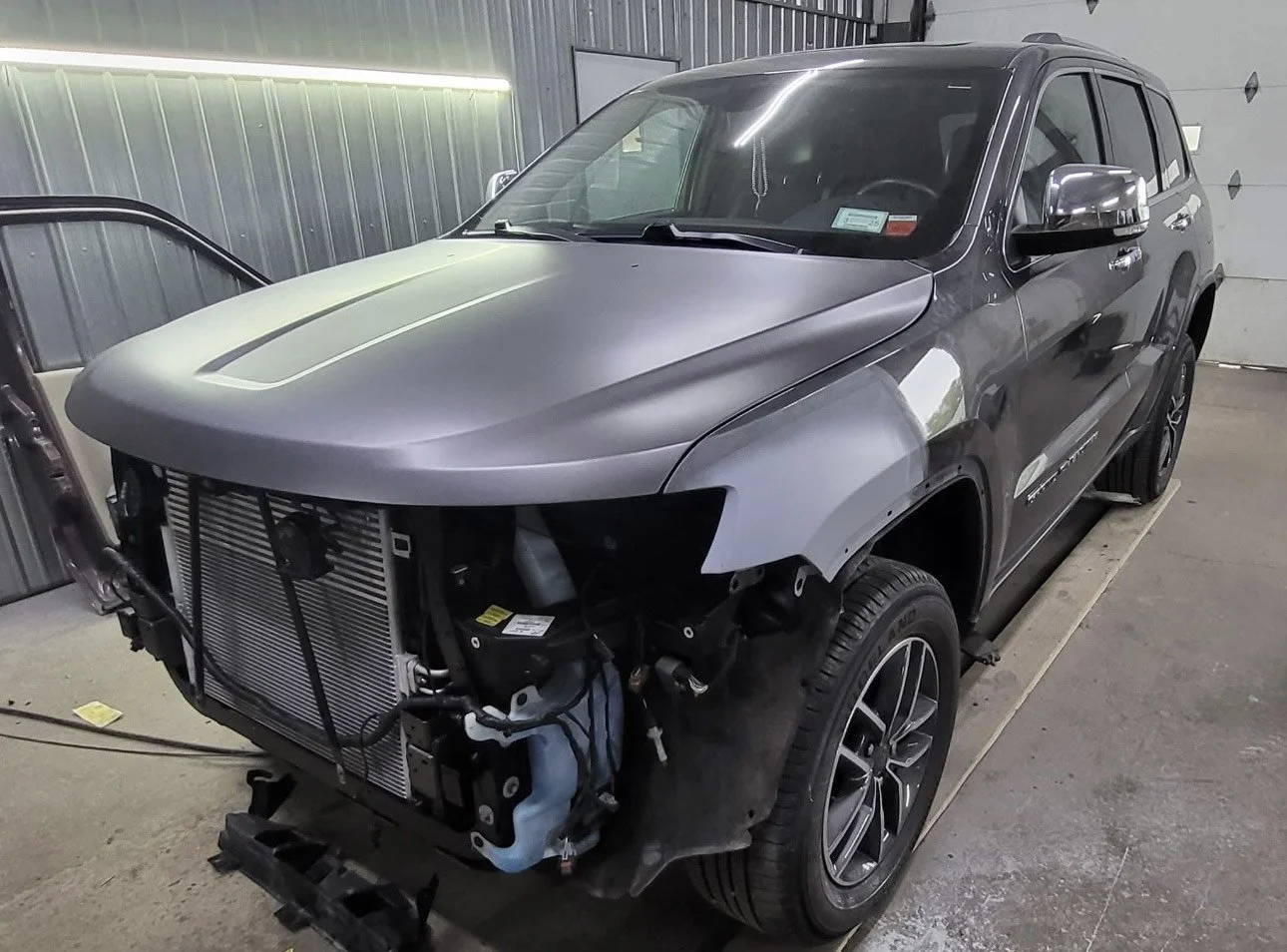 A gray SUV with front end disassembled in a garage, exposing the radiator and internal components.
