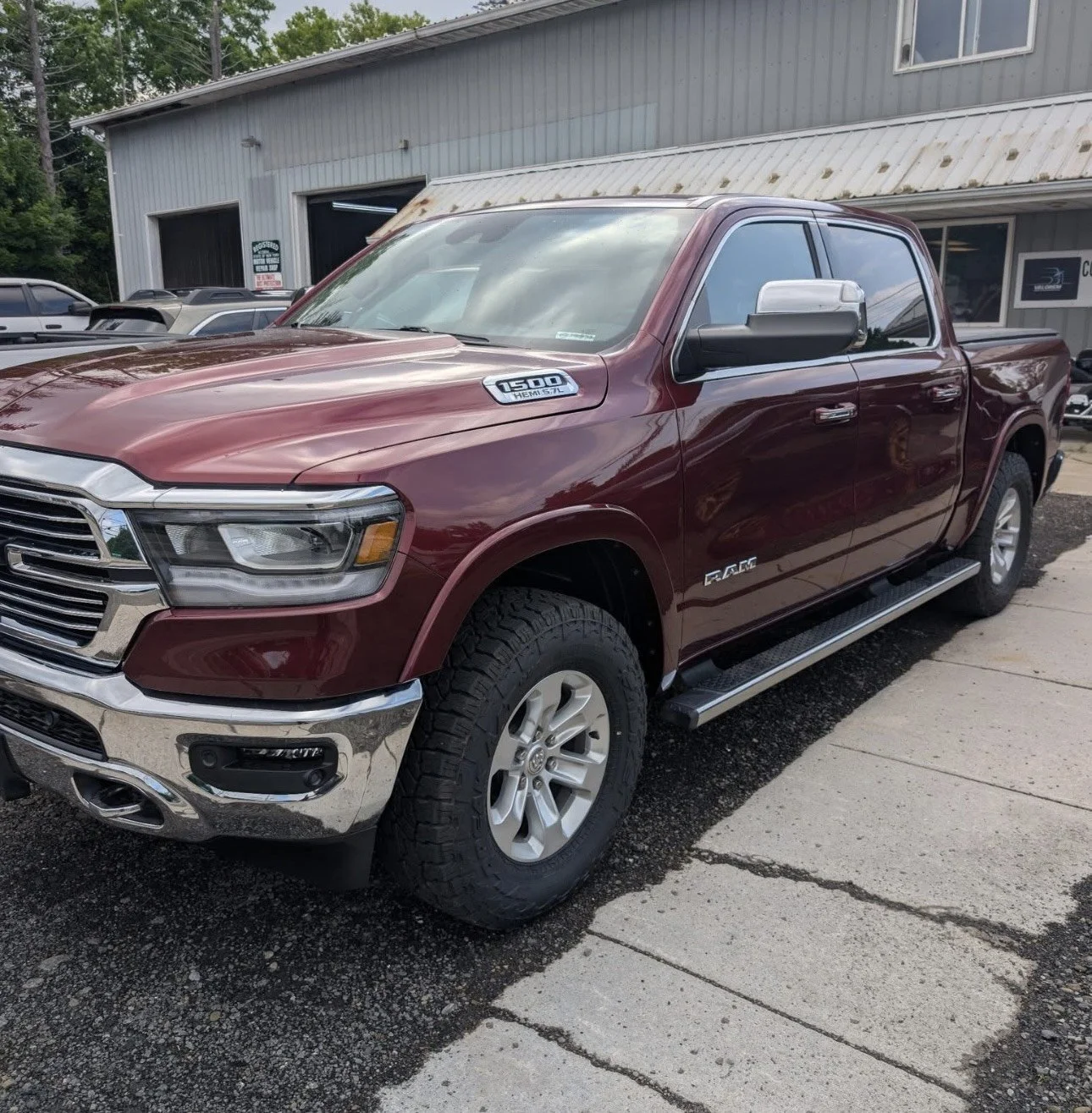Red Ram 1500 pickup truck parked outside a building with a garage and other vehicles visible in the background.