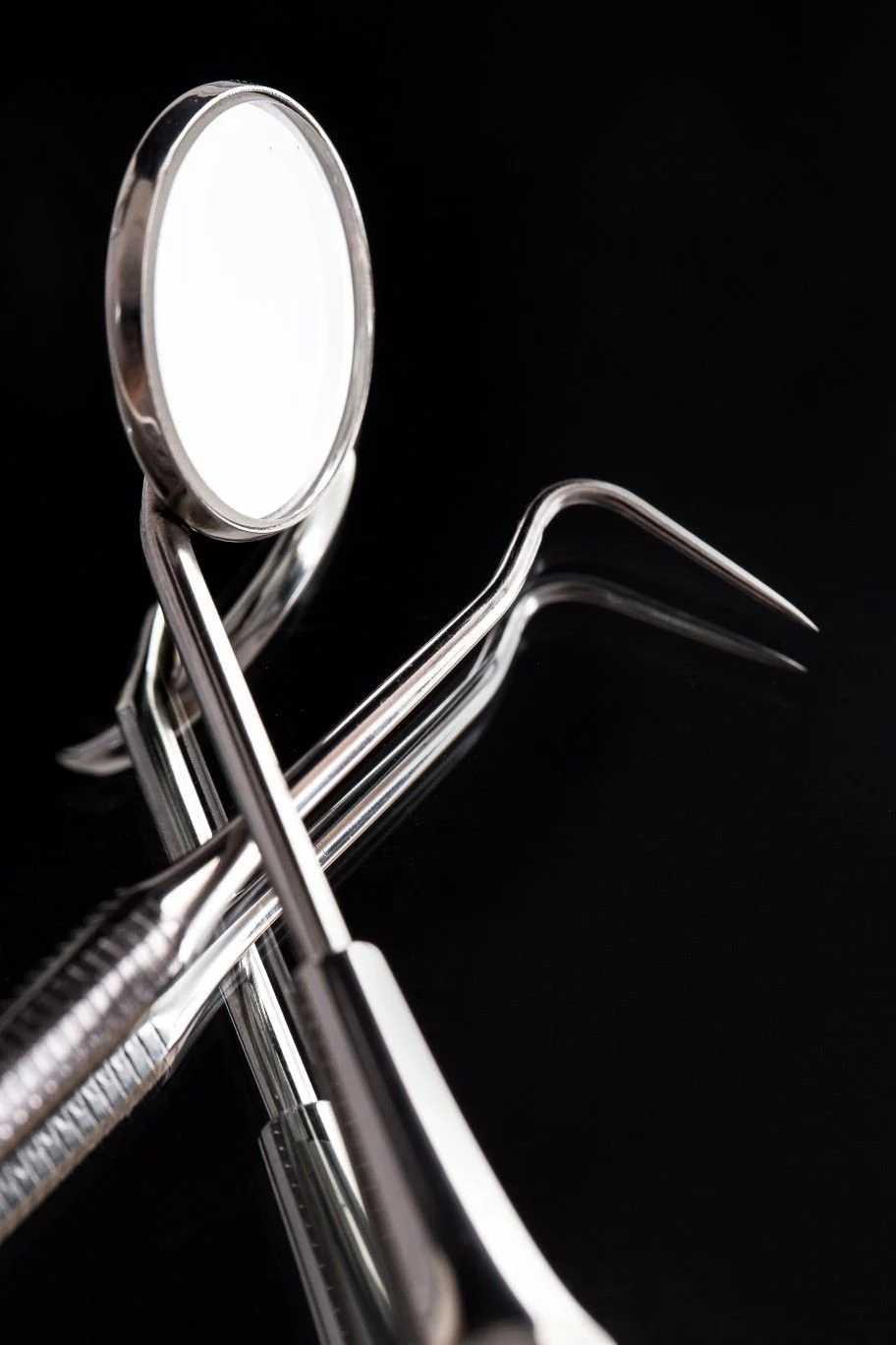 Conjunto de instrumentos dentales de acero inoxidable, incluyendo espejo, espátula y trinquete, sobre fondo negro.