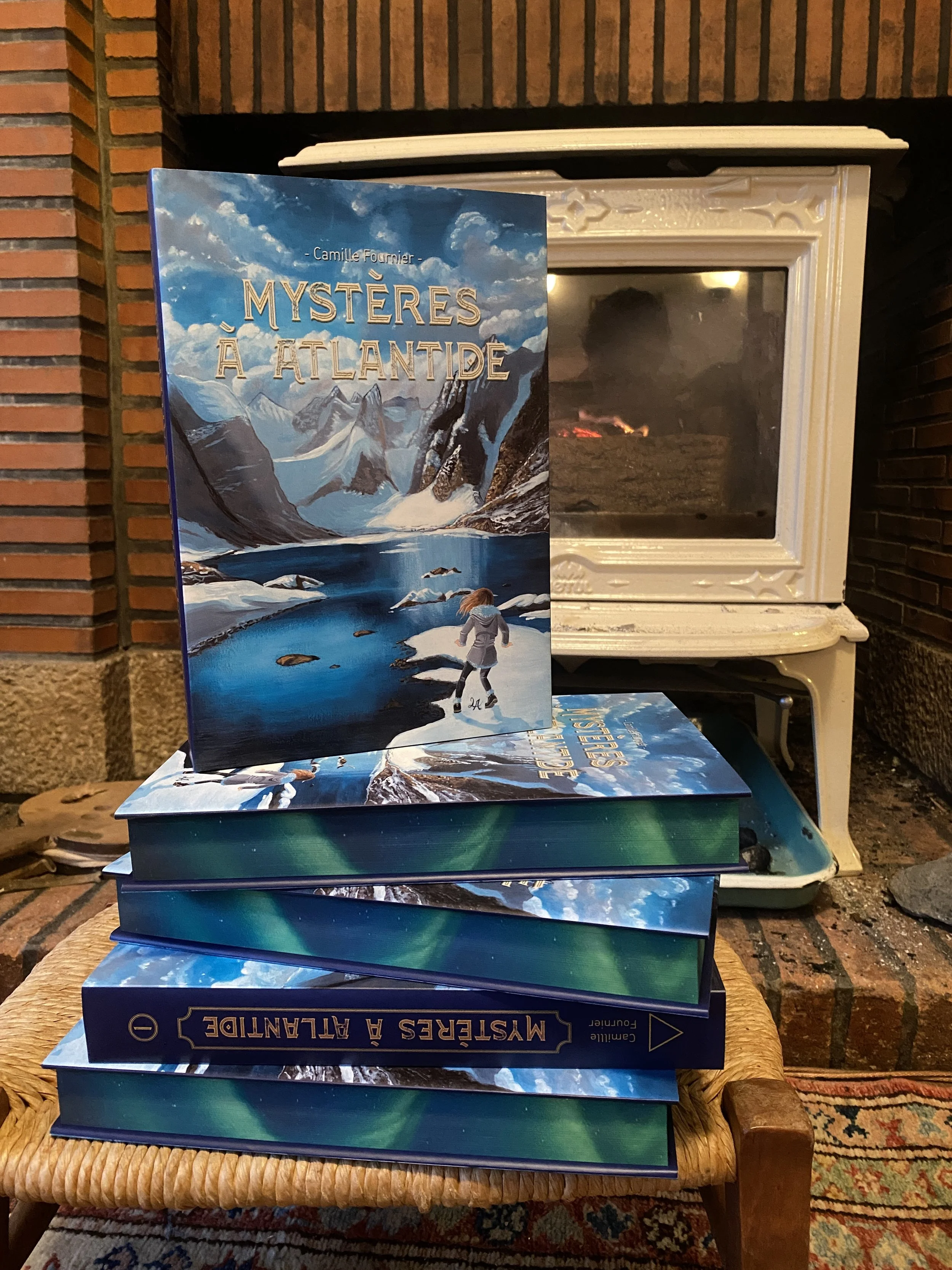 Livres empilés et un livre ouvert avec une couverture illustrée de paysages glacés, montagnes, et une personne marchant dans la neige devant une cheminée en arrière-plan.