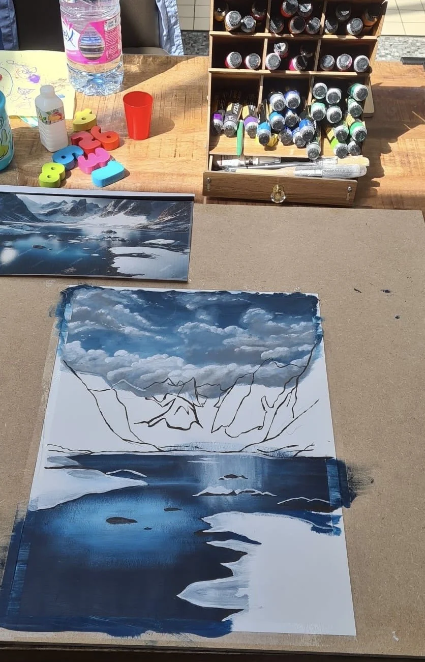 Une peinture en cours représentant un paysage de montagnes et d'eau, avec un ciel nuageux, réalisée à l'aide de peintures en acrylique ou à l'huile.