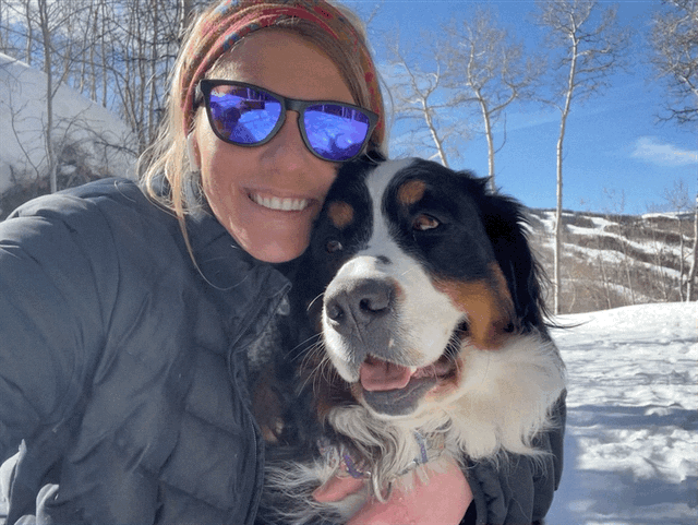 Blonde girl smiling with Bernese Mountain Dog kissing her face.