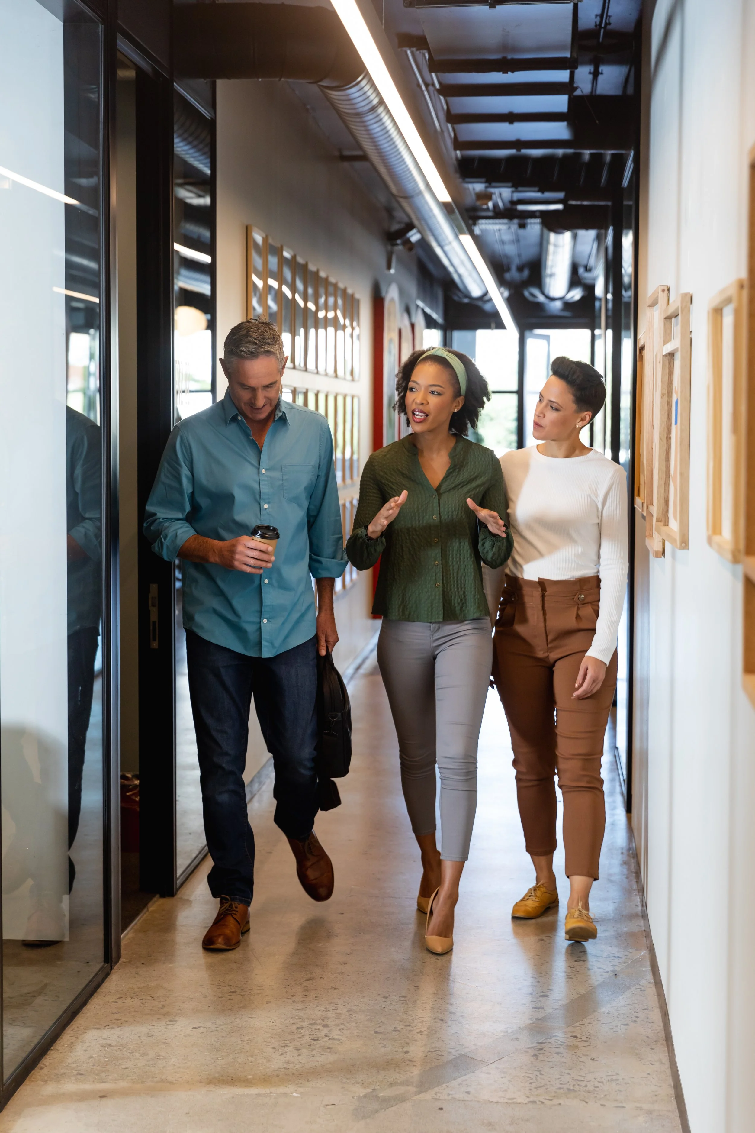 Three colleagues talking while walking down an office hallway.