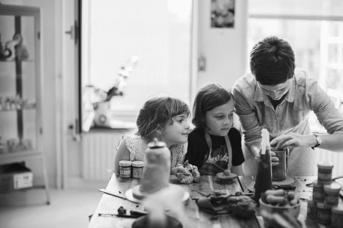 A man and two young girls in a kitchen preparing food at a table with various condiments and jars