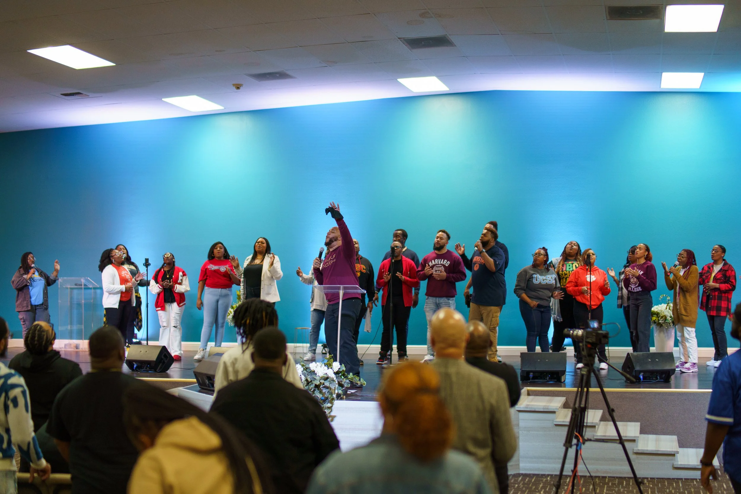 Group of people singing and praying on stage in church, with audience seated in front.