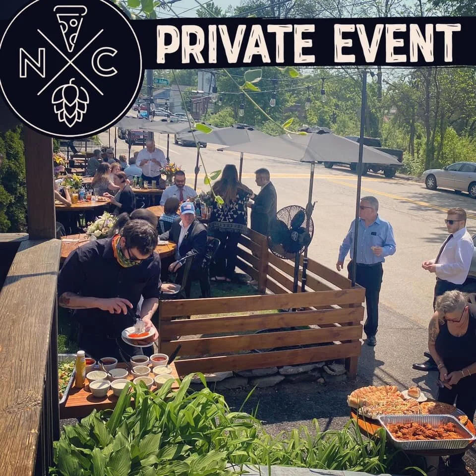 People attending a private outdoor event at a restaurant or cafe, with tables, umbrellas, and food, on a sunny day.