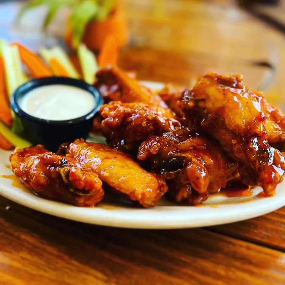 Plate of glazed chicken wings with a side of vegetable sticks and dipping sauce