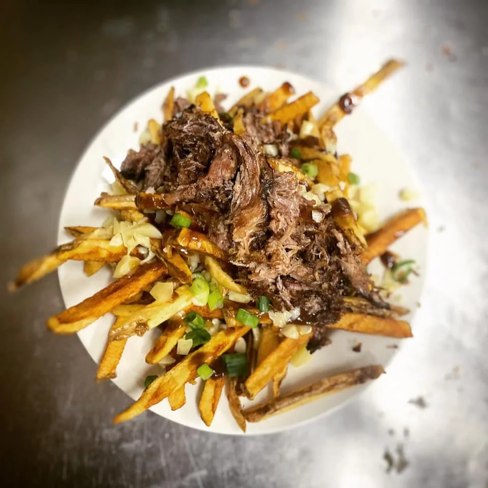 Plate of pulled beef on a bed of fries topped with chopped onions and green onions.