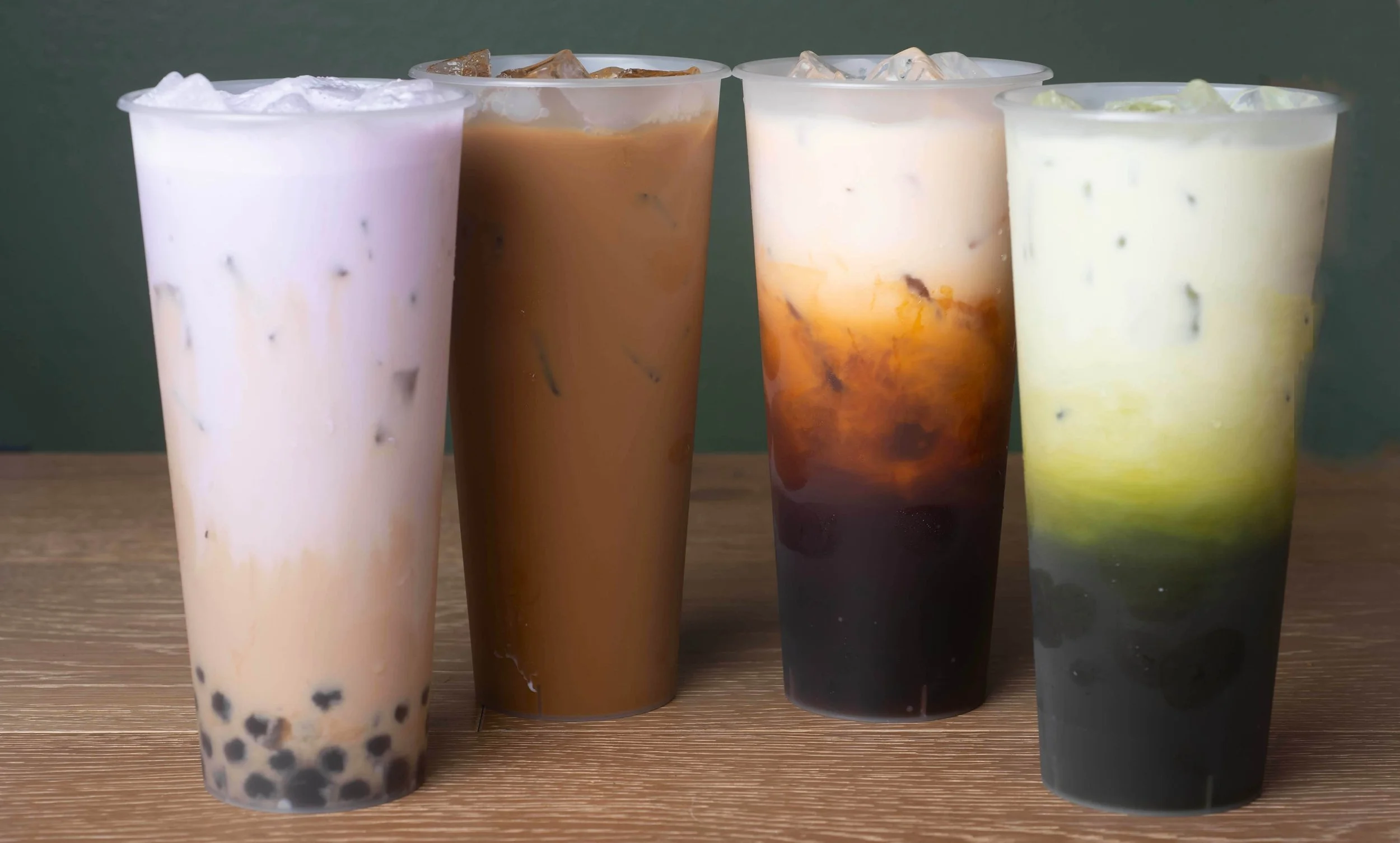 Four large cups of bubble tea with different colors and toppings on a wooden surface.